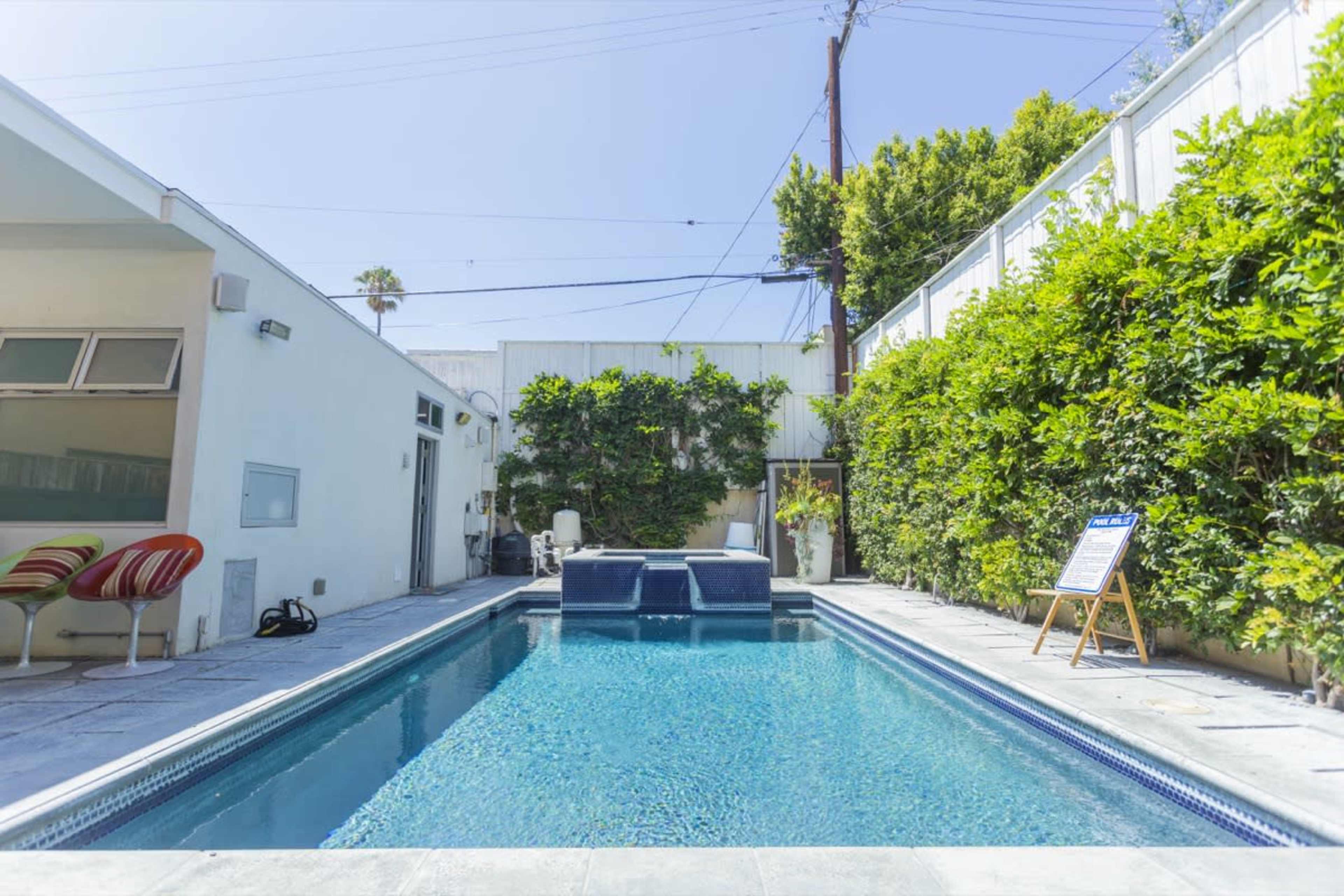 A rectangular swimming pool surrounded by greenery and a patio area with lounge chairs.