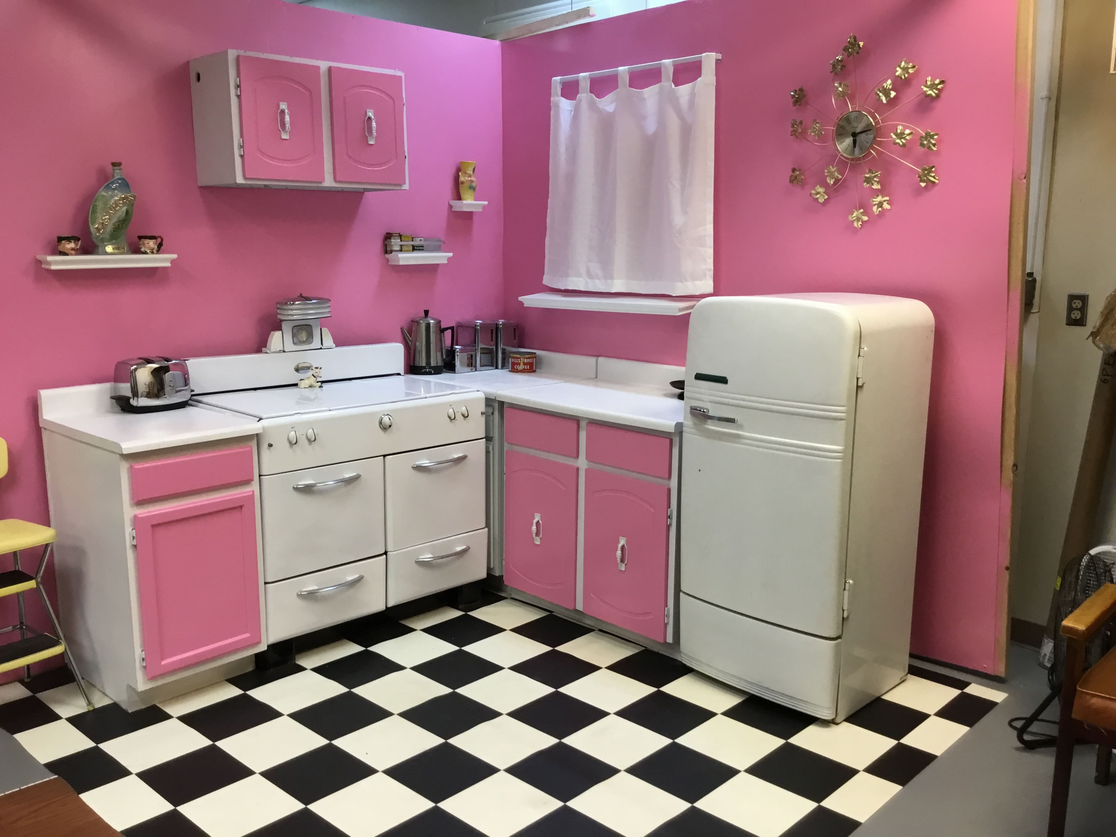 A vintage-style kitchen with pink walls, a checkered black and white floor, and white appliances, including a fridge and stove.