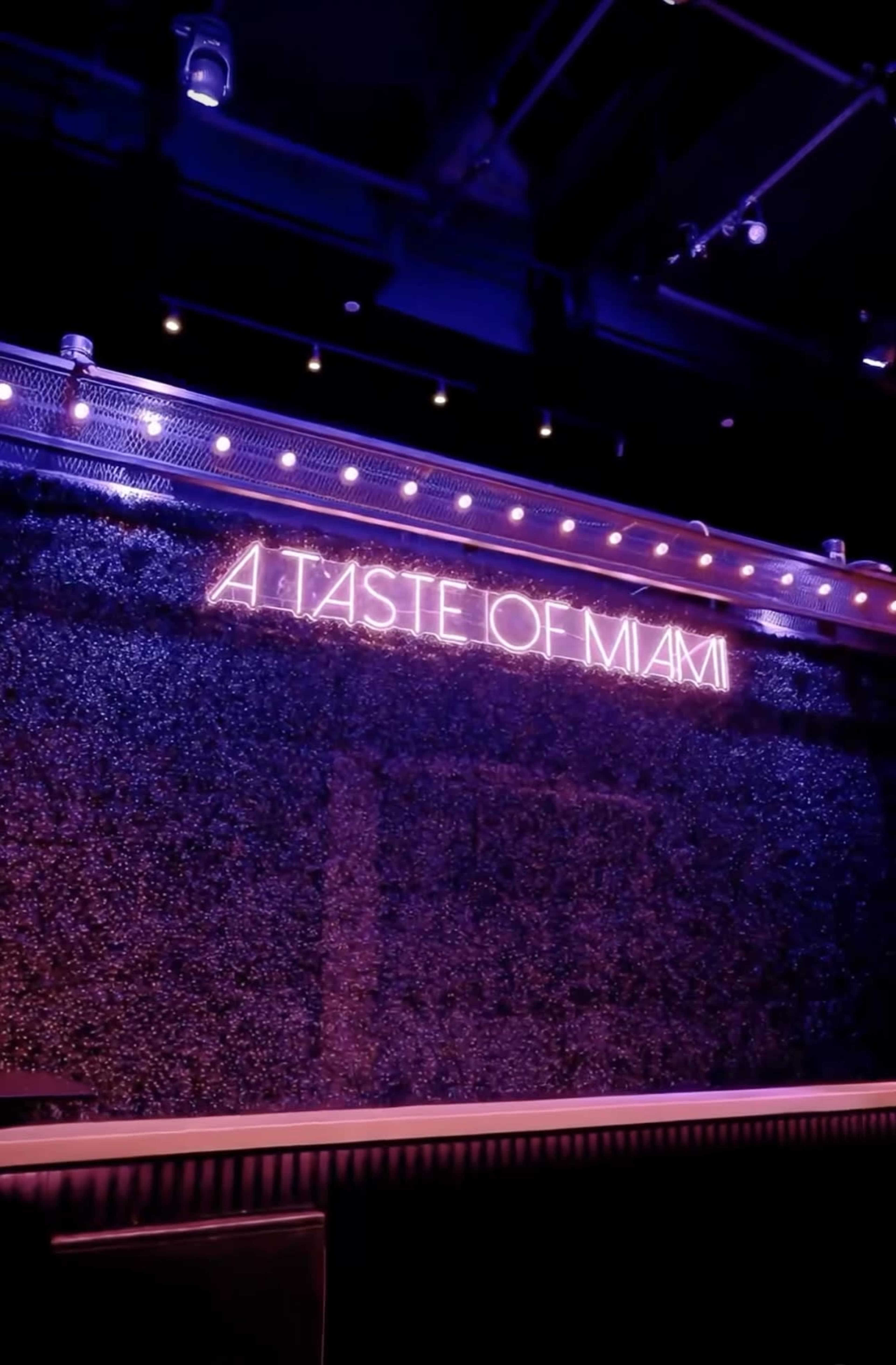 The image shows a vibrant wall adorned with a neon sign that reads "A Taste of Miami."