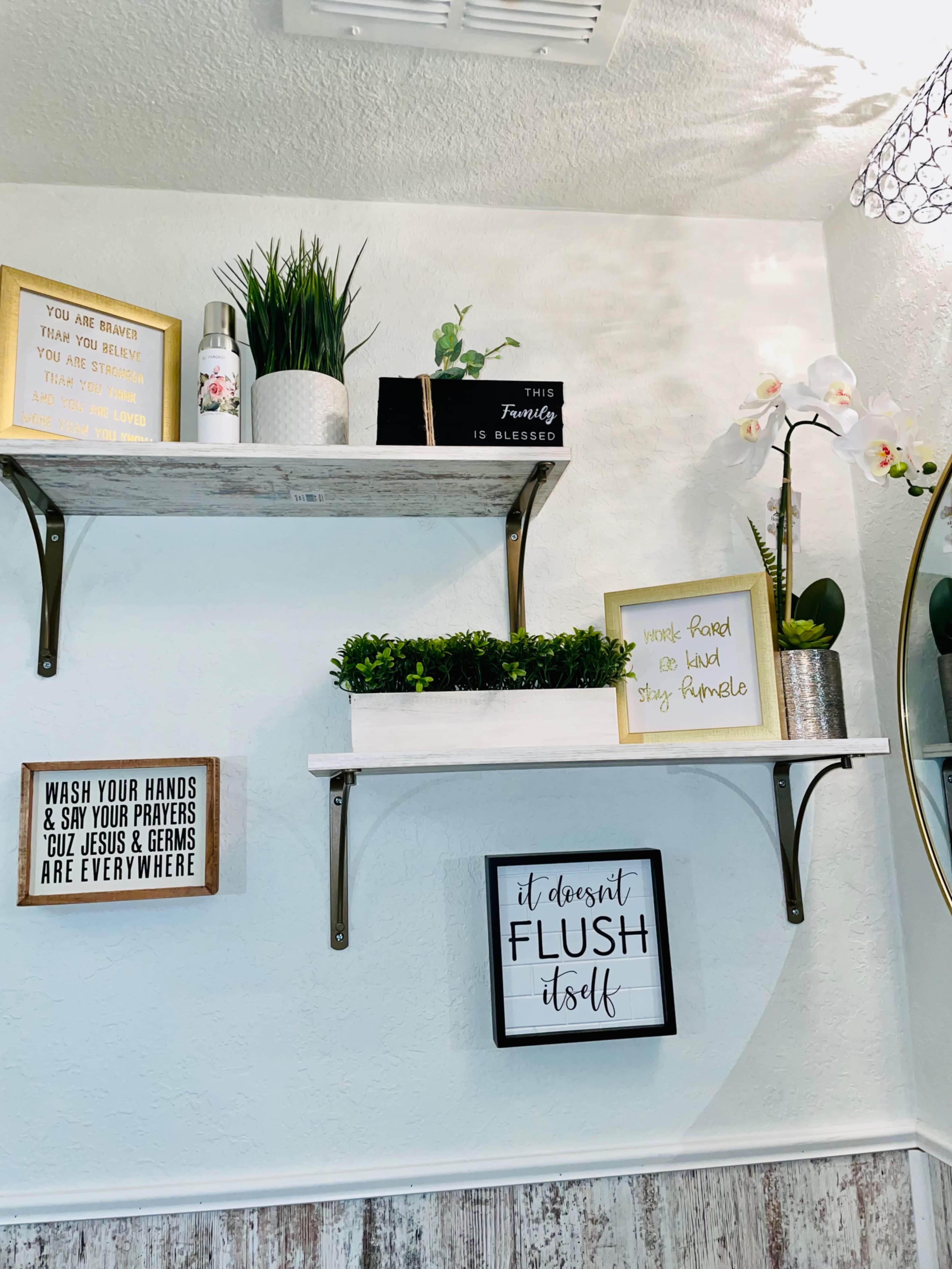 Two wall-mounted shelves displaying various decorative signs, plants, and a round mirror in a well-lit room.