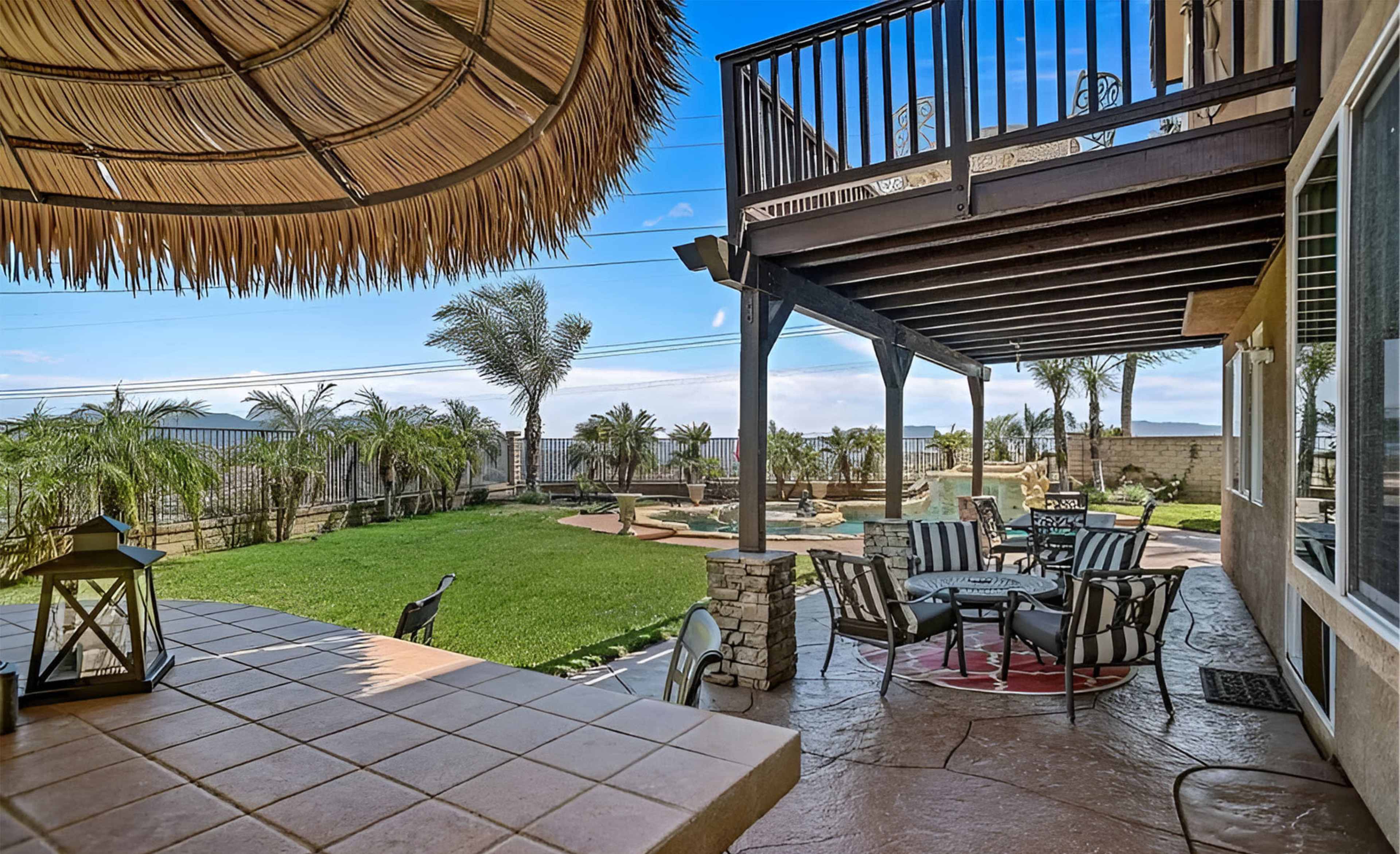 The image shows a patio area featuring outdoor seating and a large lawn with palm trees in the background.
