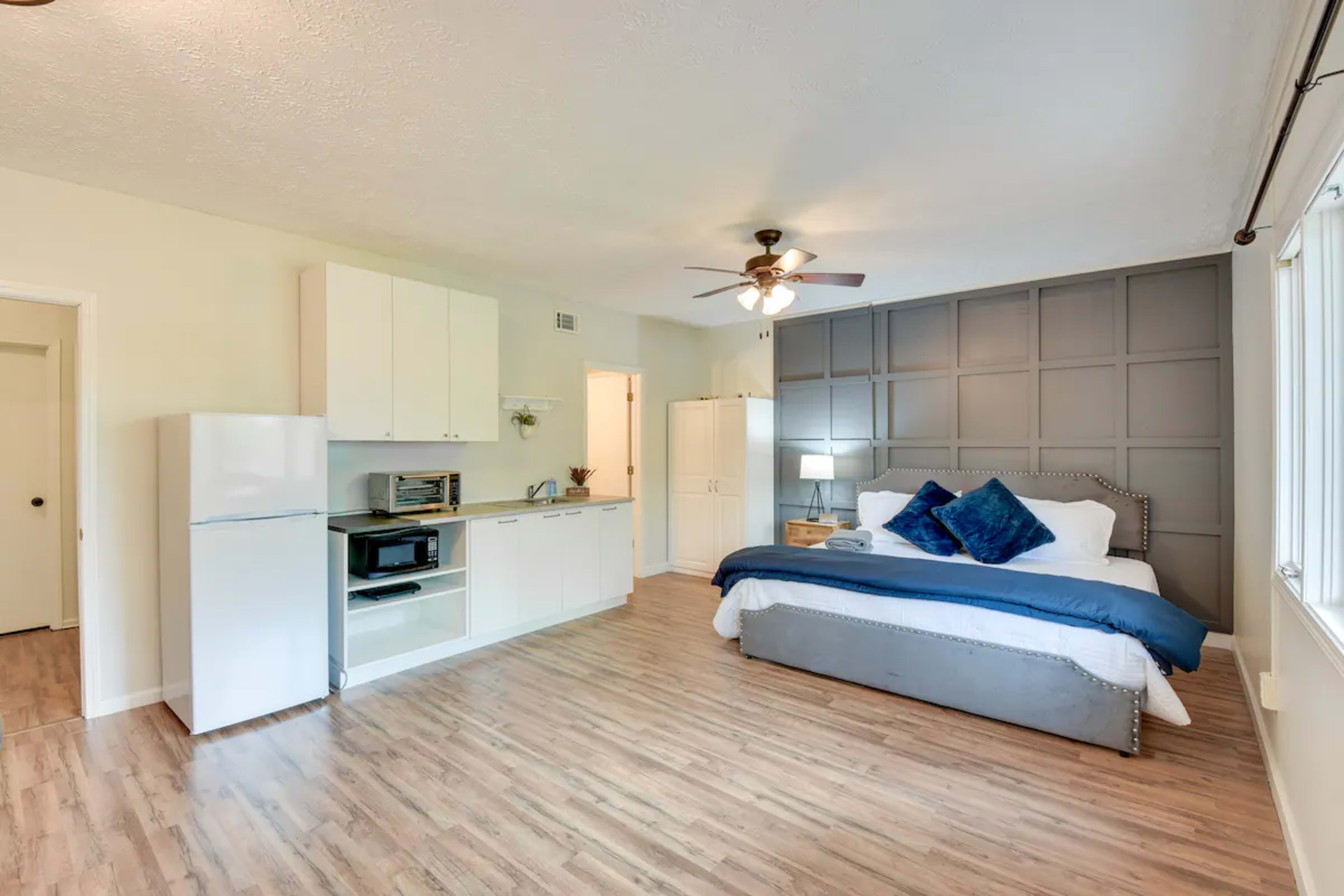A spacious bedroom featuring a king-sized bed, a kitchenette with a refrigerator and microwave, and large windows allowing for natural light.