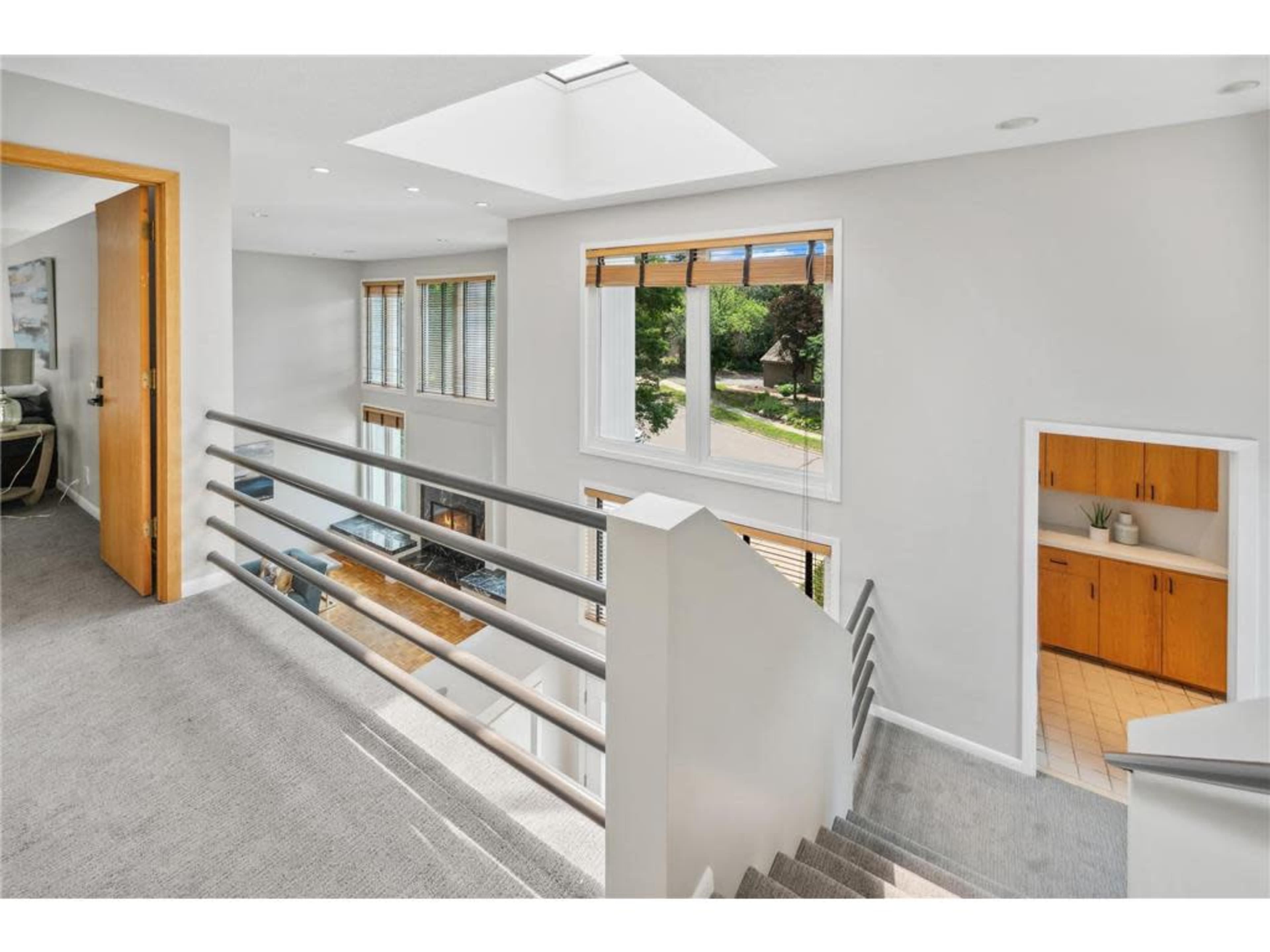 A bright, modern staircase leads to an open upper level with large windows and a view of the exterior landscape.