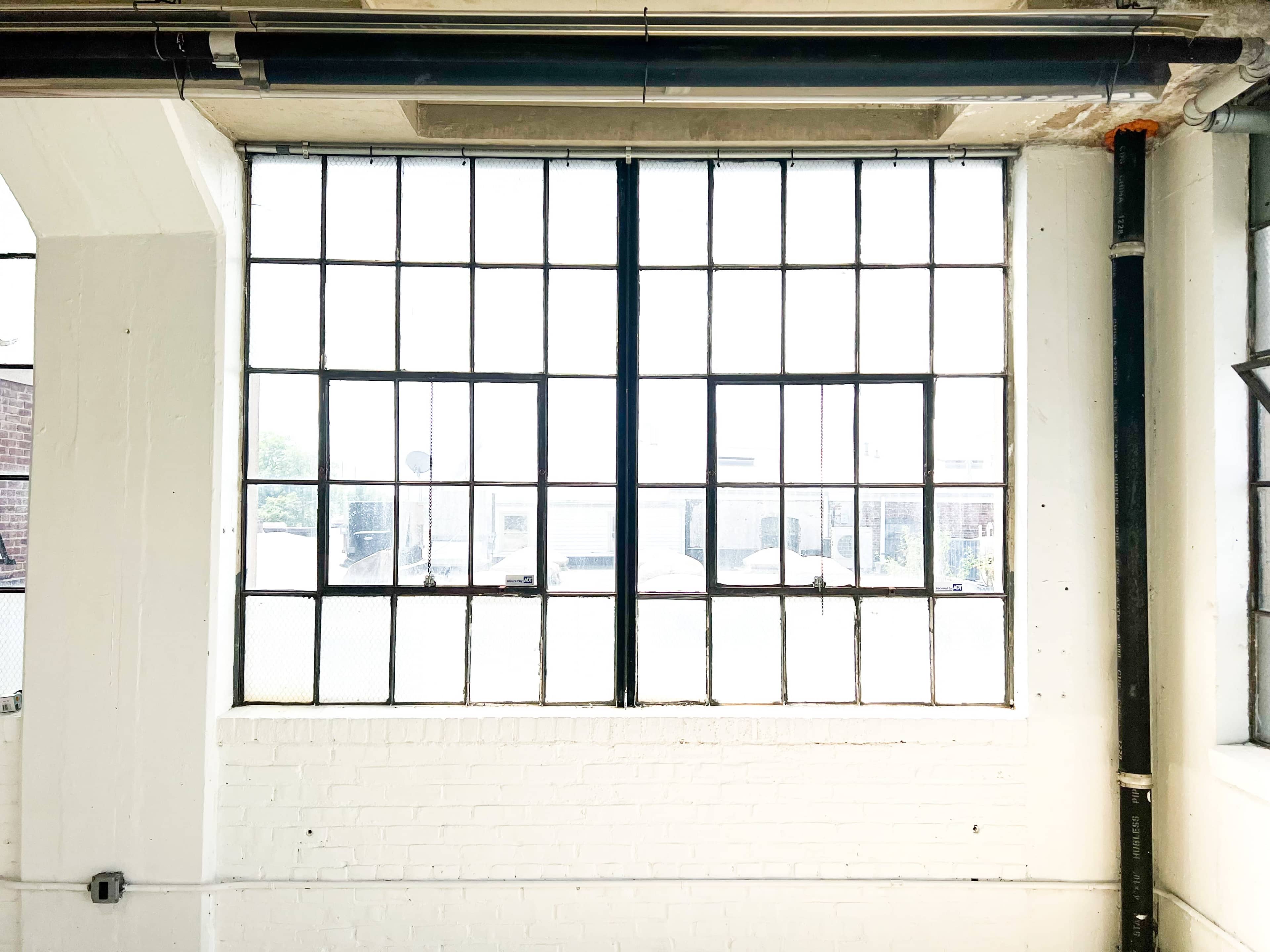 A large industrial window with multiple panes set in a white brick wall.