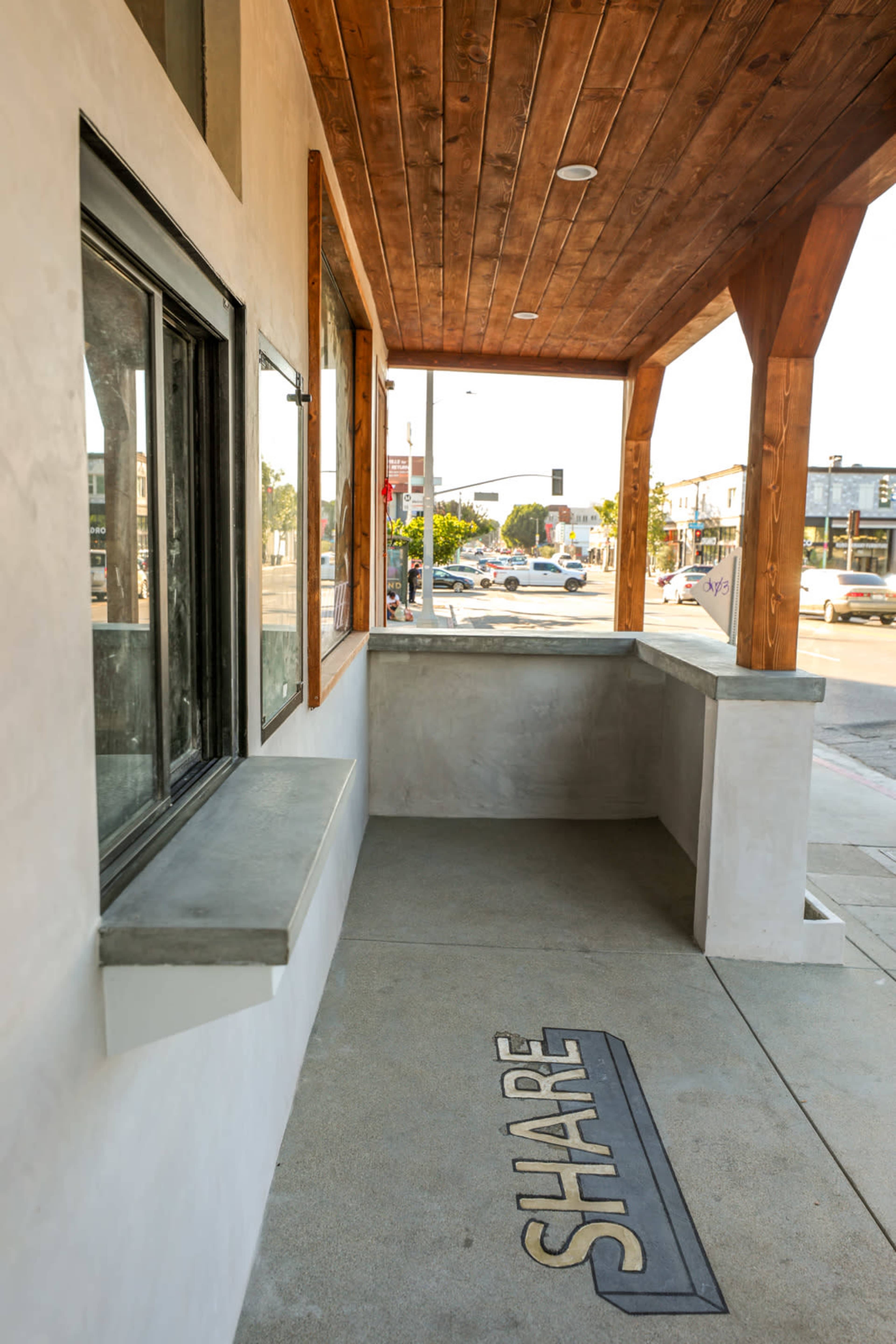 A concrete porch with a wooden ceiling and the word "SHARE" emblazoned on the ground, overlooking a street with traffic signals in the background.