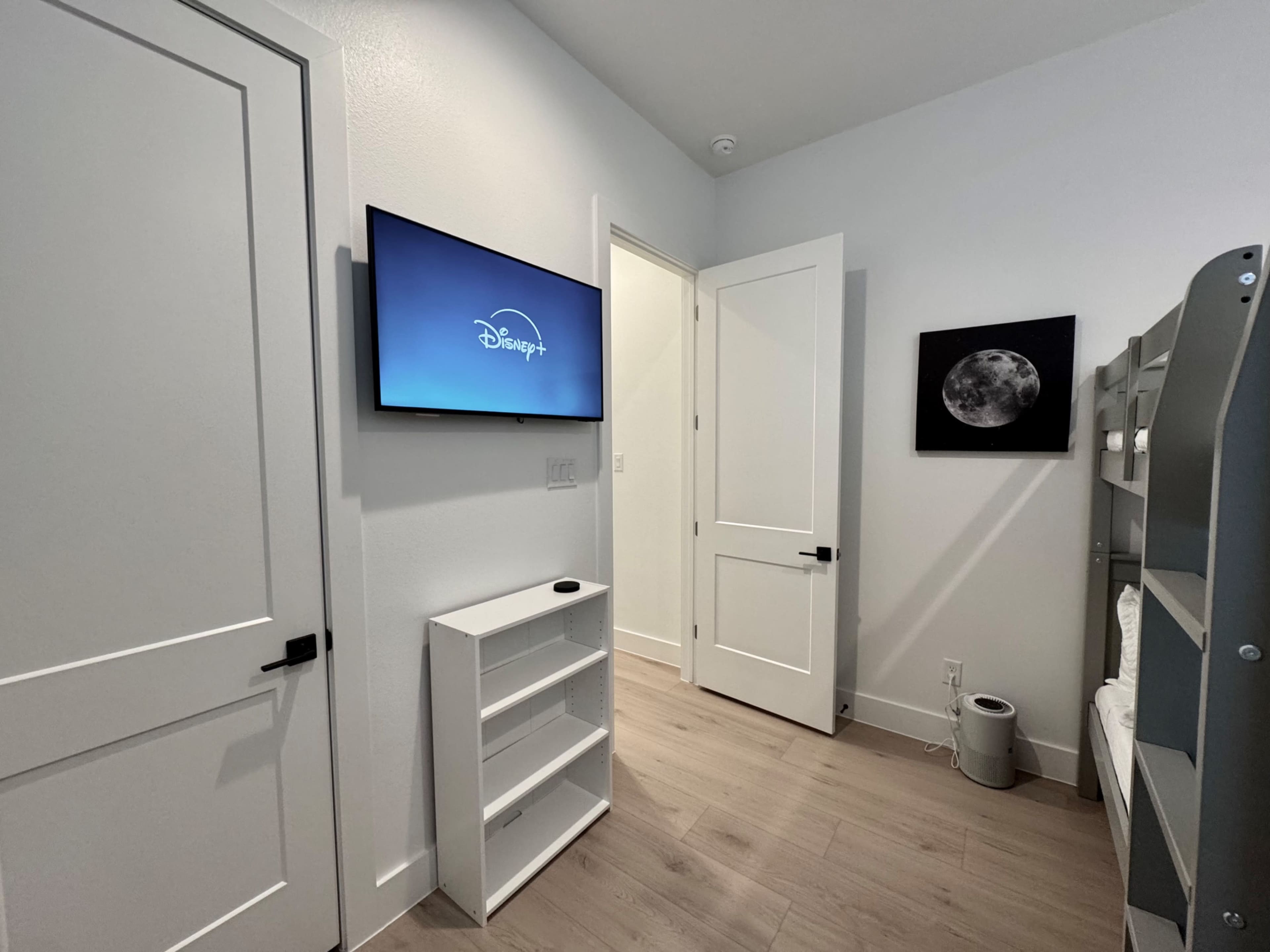 The image shows a small room with a television displaying the Disney logo, a white shelf, a door leading to another room, and a moon picture on the wall.