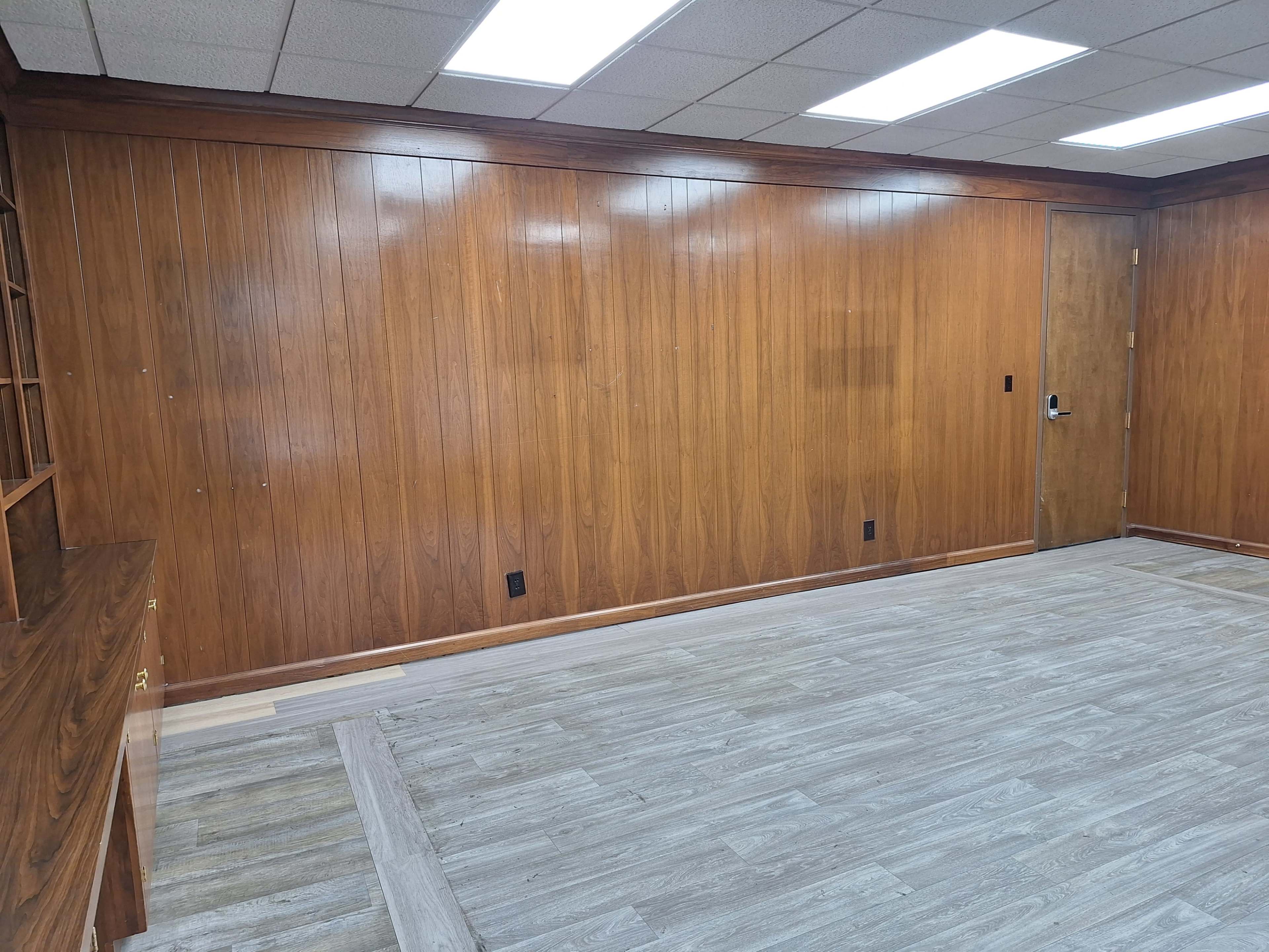 The image shows a room with wooden paneling on the walls, a door on the right, and light-colored flooring.