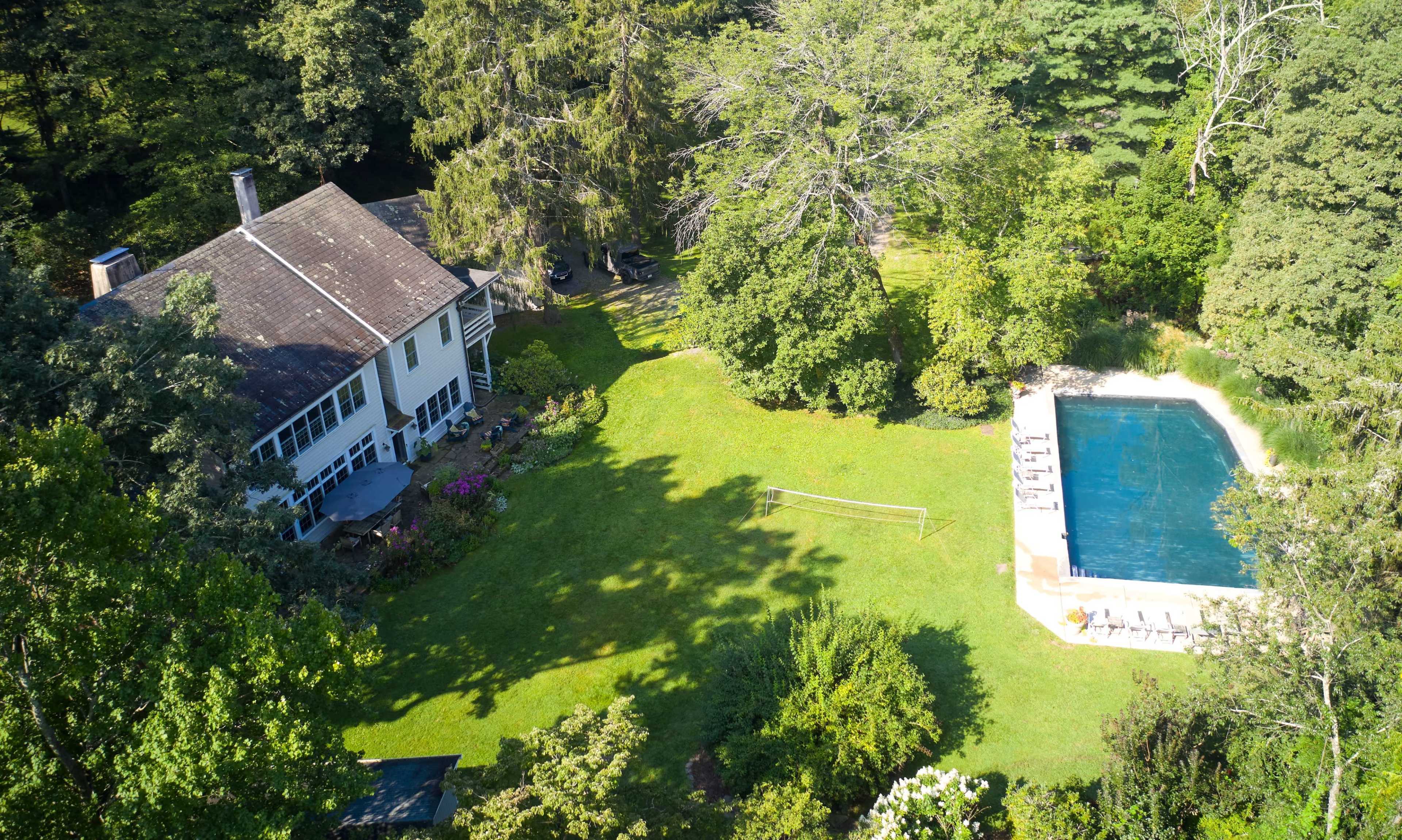 A large house surrounded by trees and a meticulously maintained lawn, featuring a swimming pool on one side.