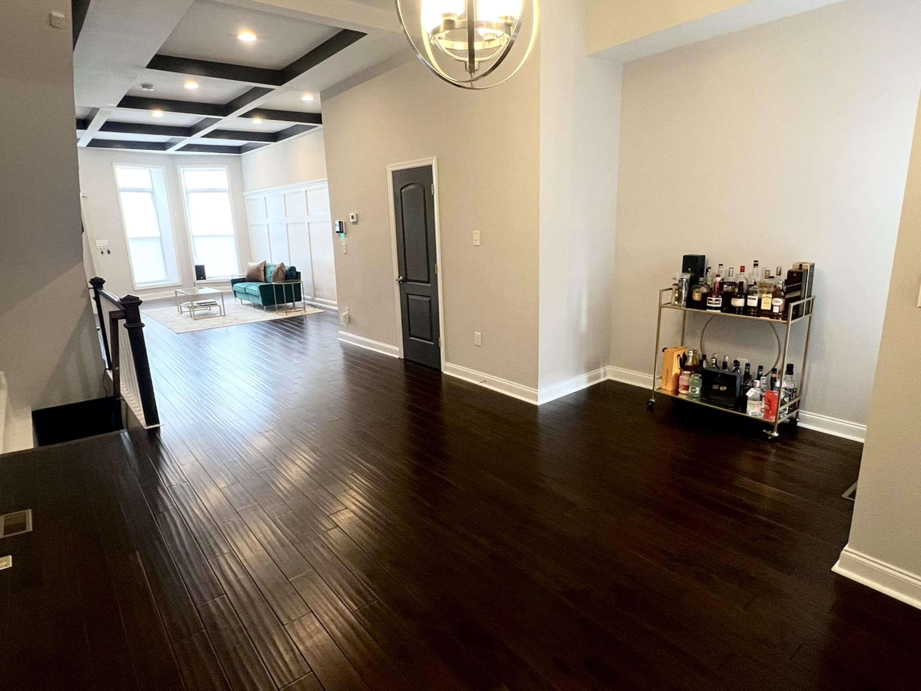 A spacious, well-lit interior with dark wooden flooring, a seating area, and a bar cart against the wall.