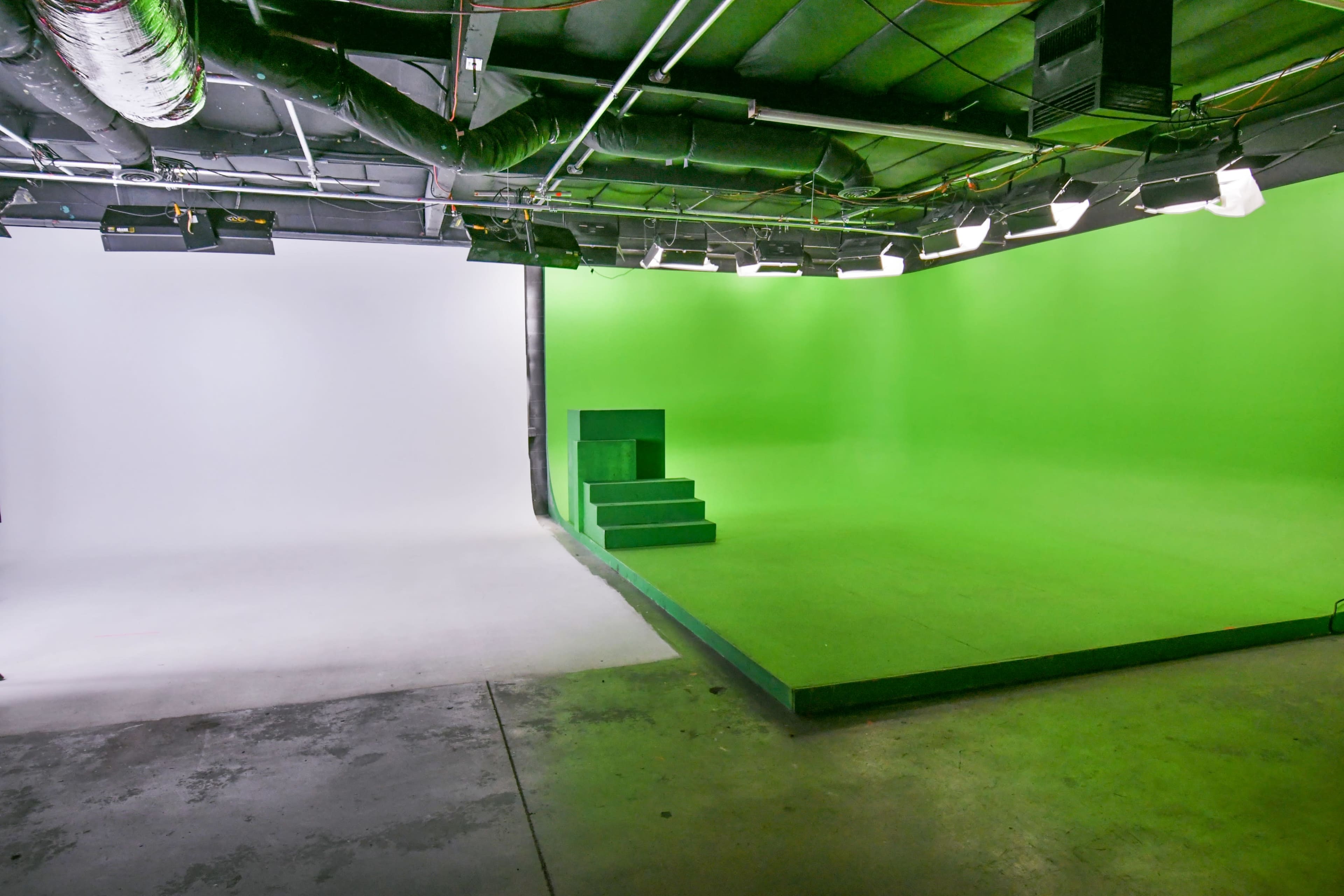 A studio space divided between a white backdrop on one side and a green screen with a raised platform on the other side.