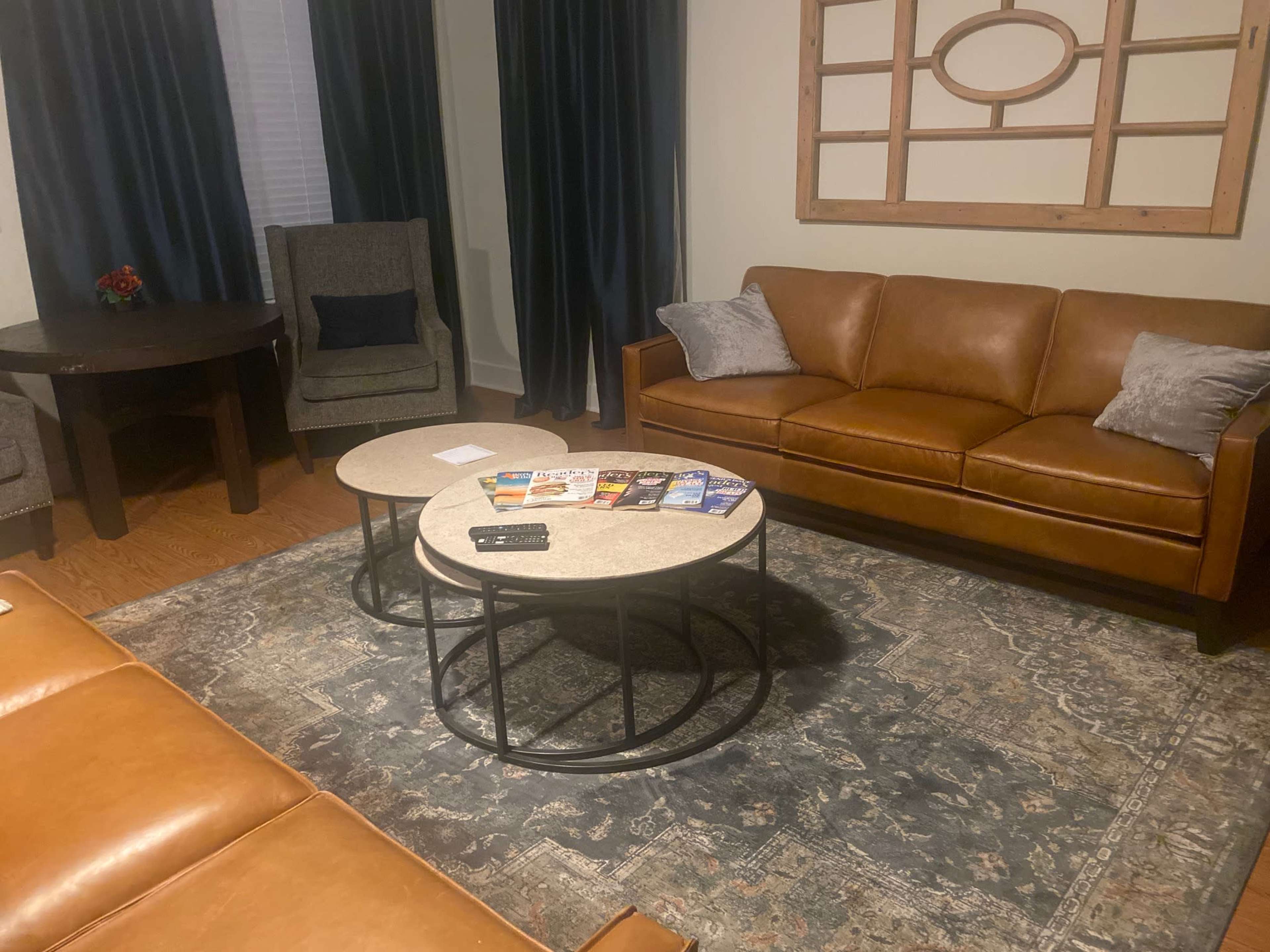 A living room with a brown leather sofa, two coffee tables with magazines arranged on top, and a patterned rug.