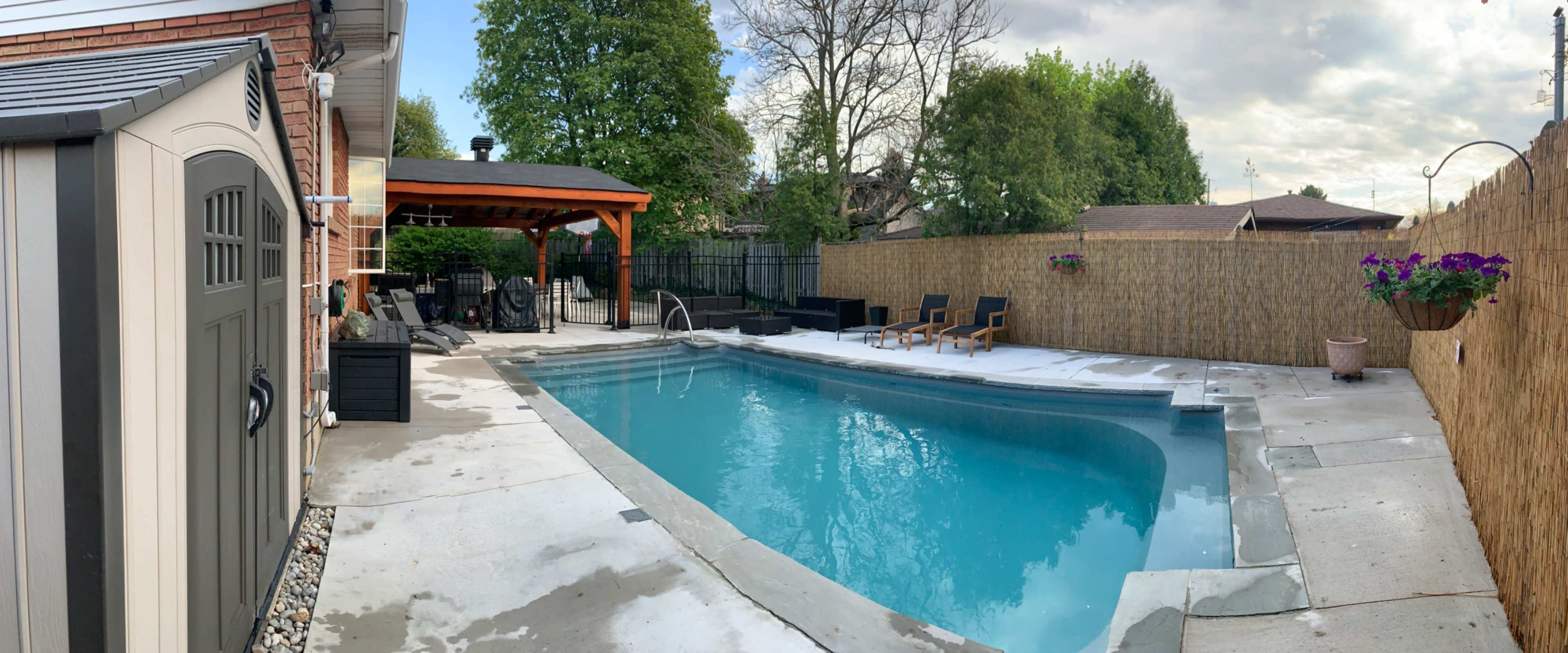 The image shows a backyard with a rectangular swimming pool surrounded by a concrete deck, patio furniture, and a gazebo.
