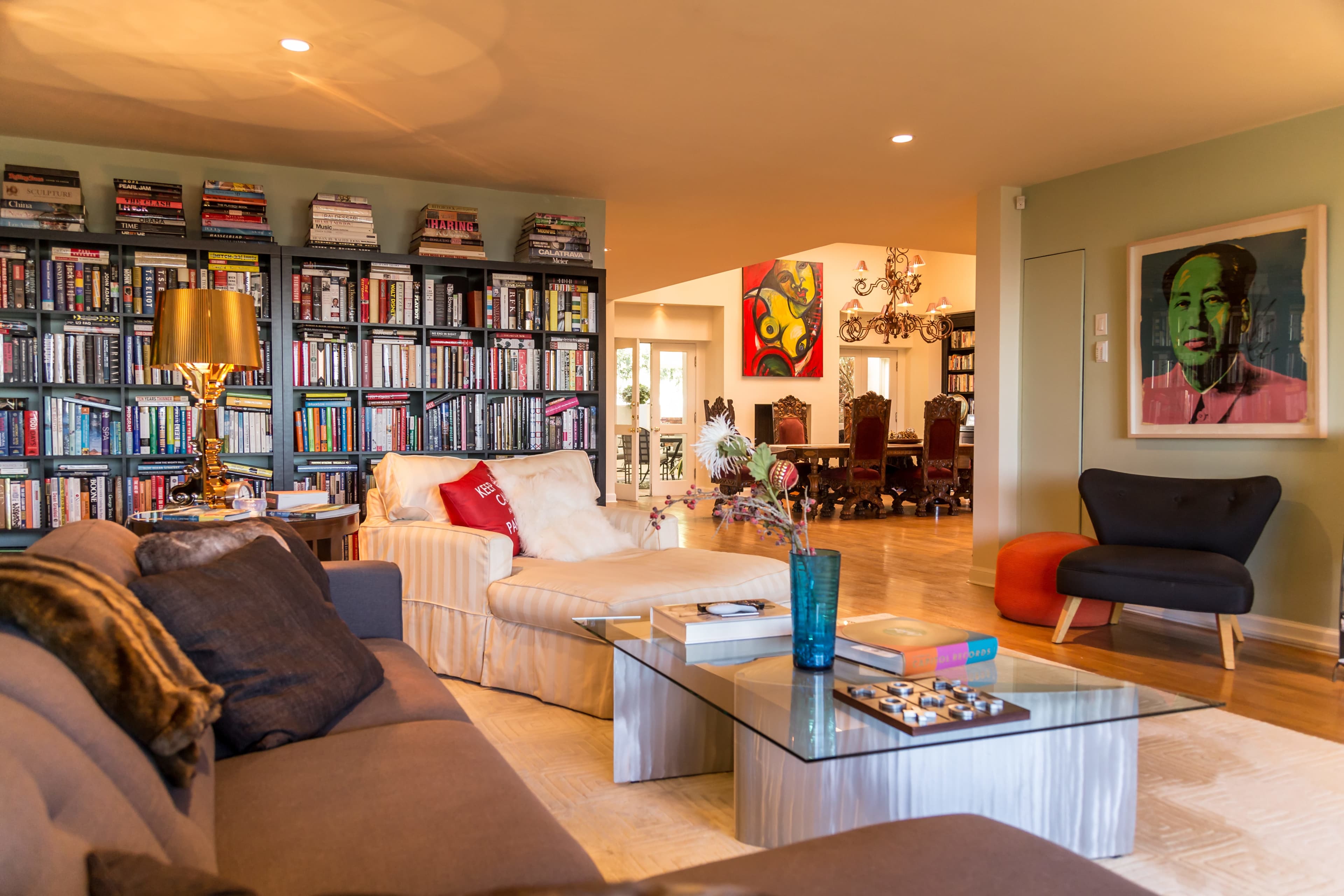 A stylish living room with a large bookshelf, a comfortable sofa, a glass coffee table, and a colorful artwork on the wall.