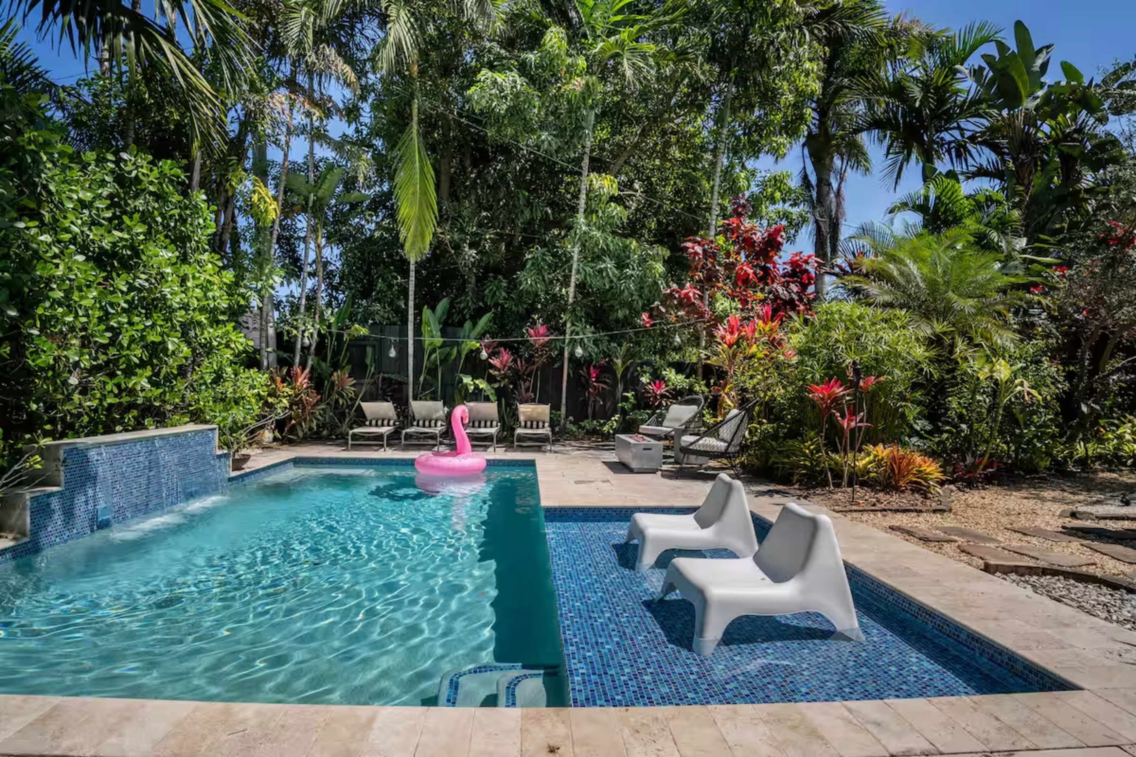 The image depicts a backyard pool surrounded by tropical plants with a pink flamingo float and lounge chairs.