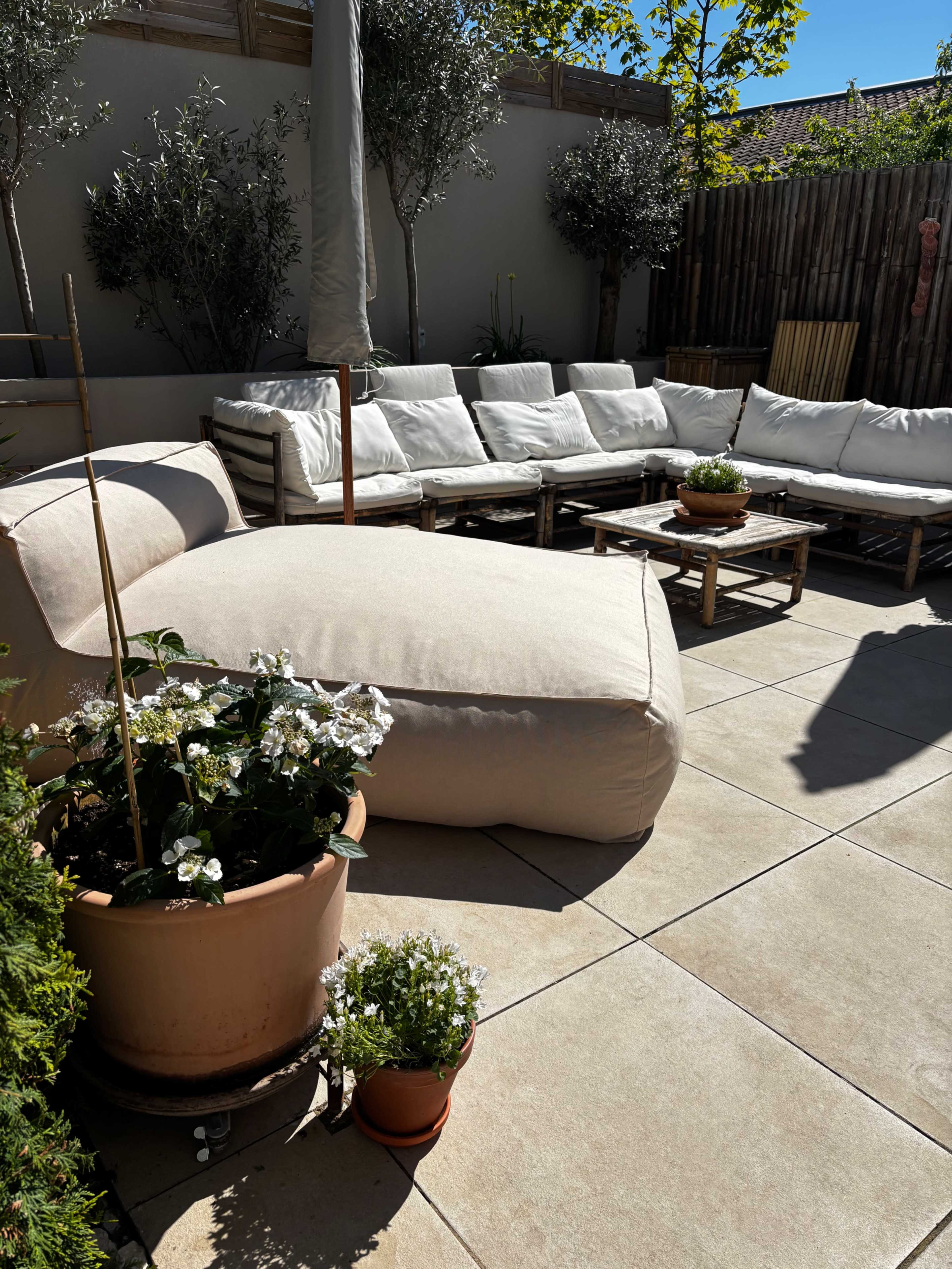 A patio area features a large, beige bean bag chair, a sectional sofa with white cushions, wooden coffee tables, and potted plants.