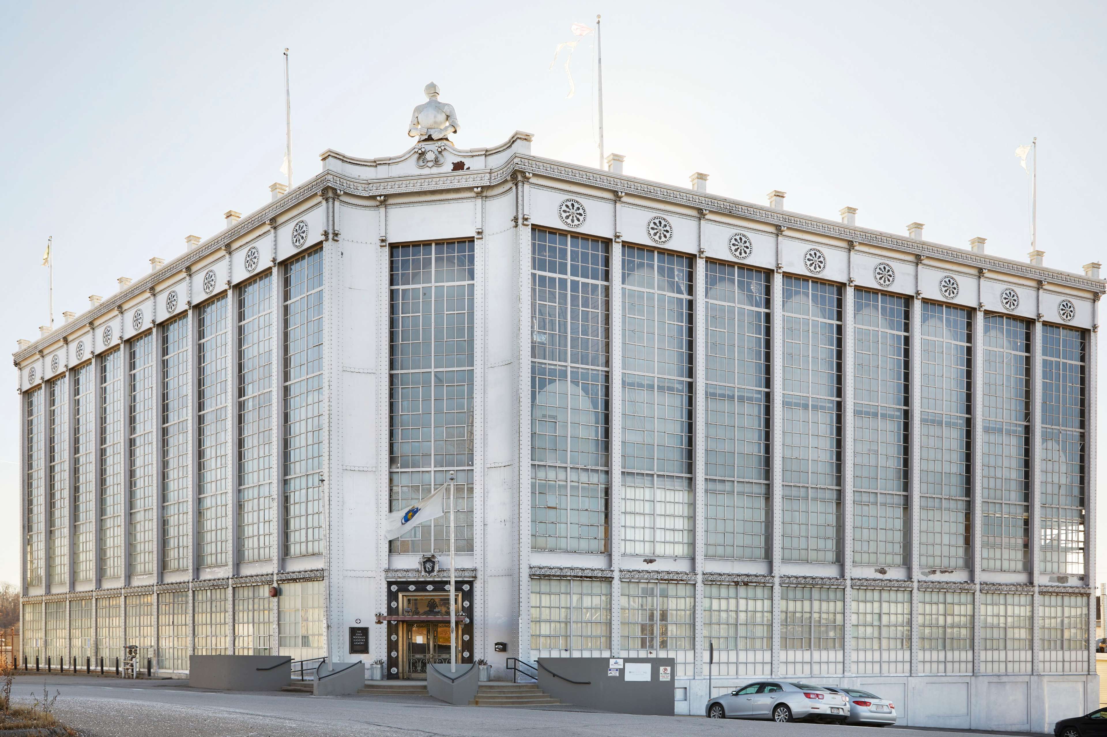 The image shows a large, modernist architectural building with a grid of large windows and a prominent figure atop the roof.