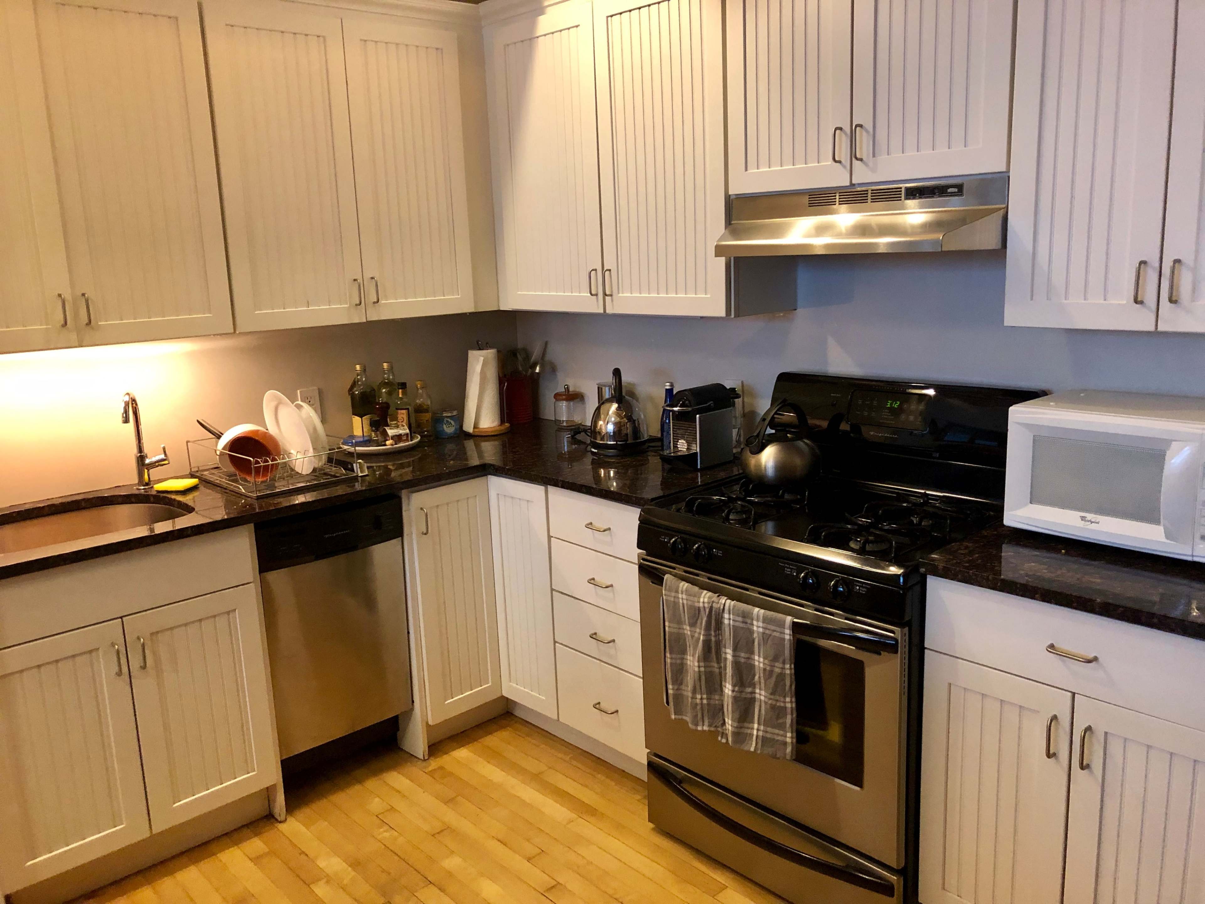 A modern kitchen with white cabinetry, a stainless steel stove, a sink, a dishwasher, and a microwave, all set against a wooden floor.