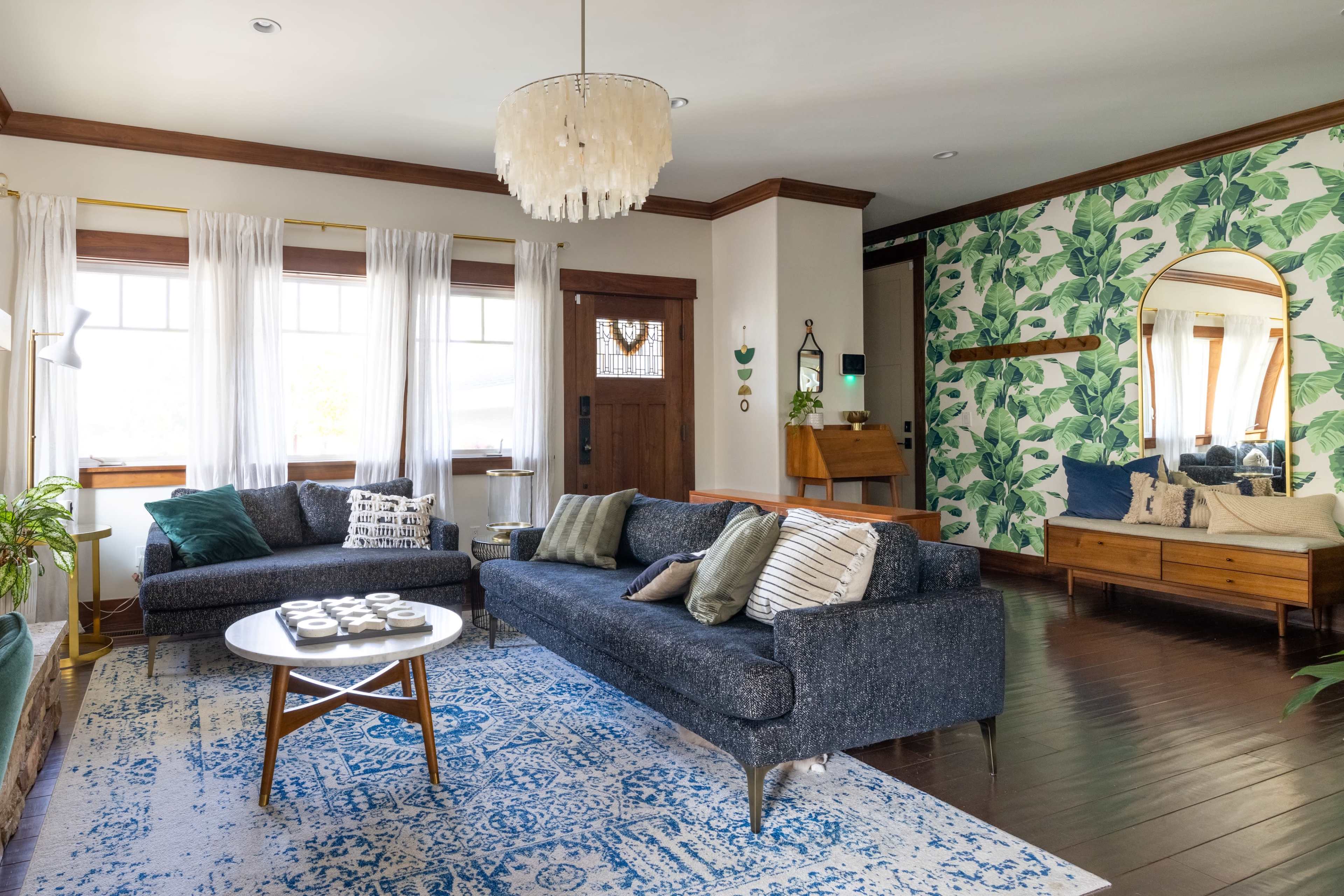 A modern living room features two dark blue sofas, a round coffee table, and a green leaf-themed accent wall.