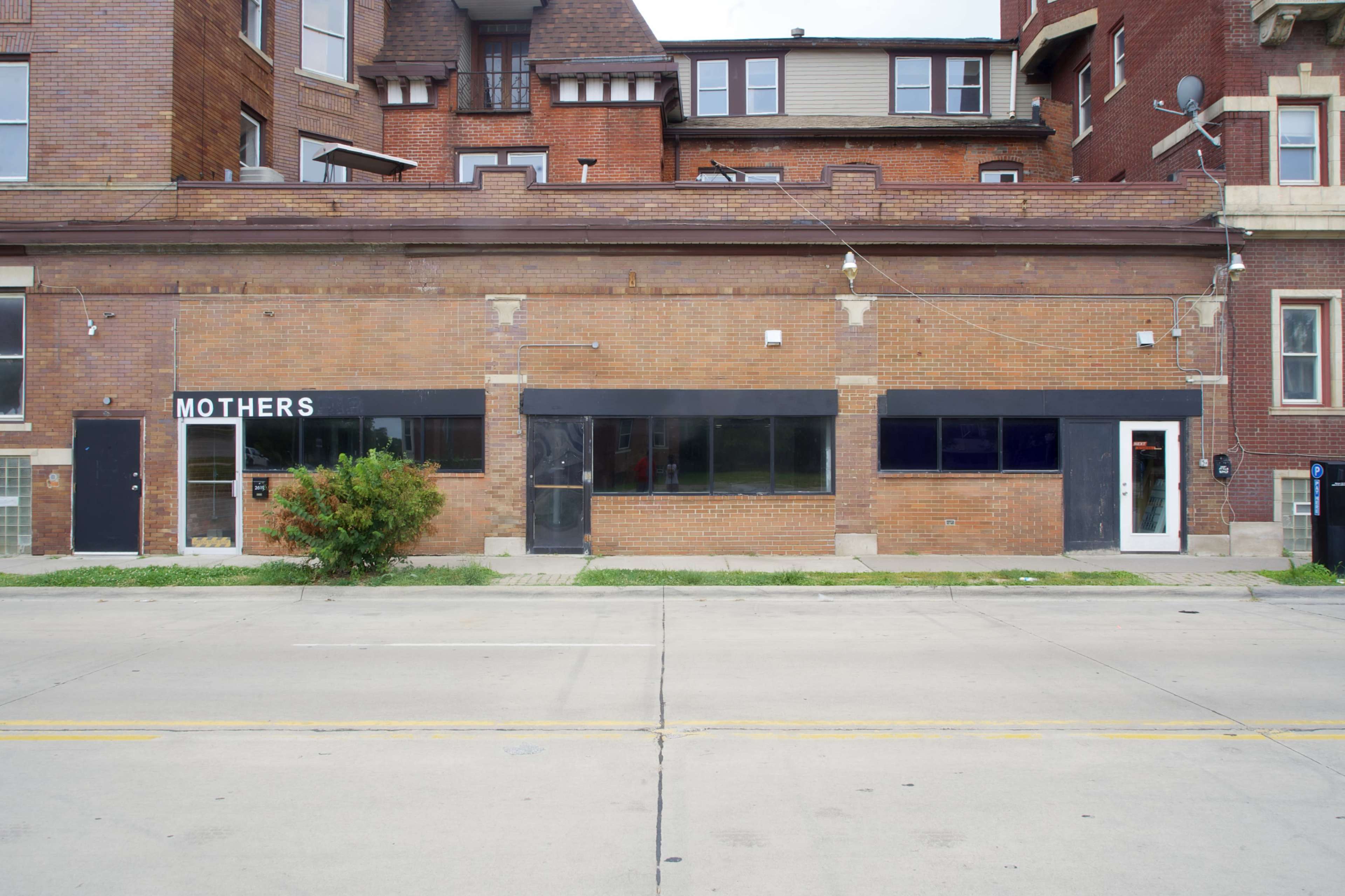 The image shows a brick building with several windows and doors, featuring a sign that reads "MOTHERS" on one side.