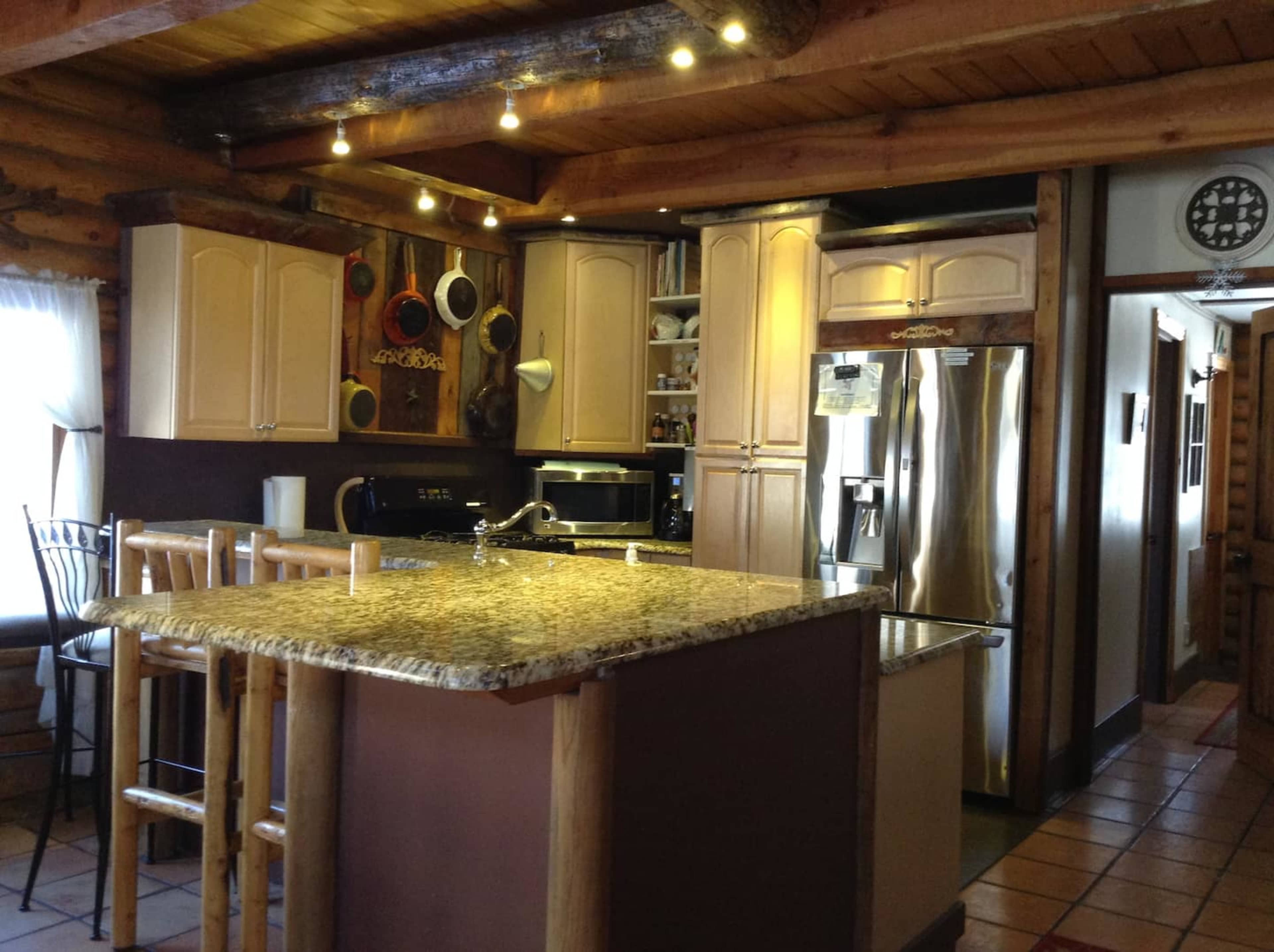 A kitchen with a central island topped with granite and wooden bar stools, surrounded by cabinetry and stainless steel appliances.