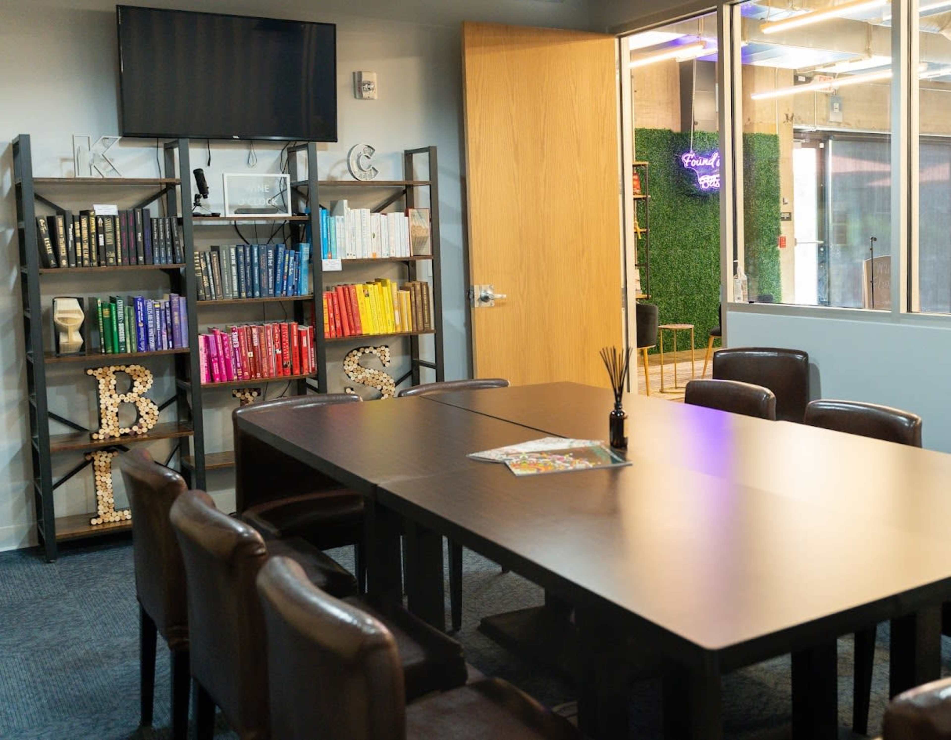 A conference room with a large table surrounded by chairs, a mounted TV, and bookshelves filled with books and decorative letters on the shelves.