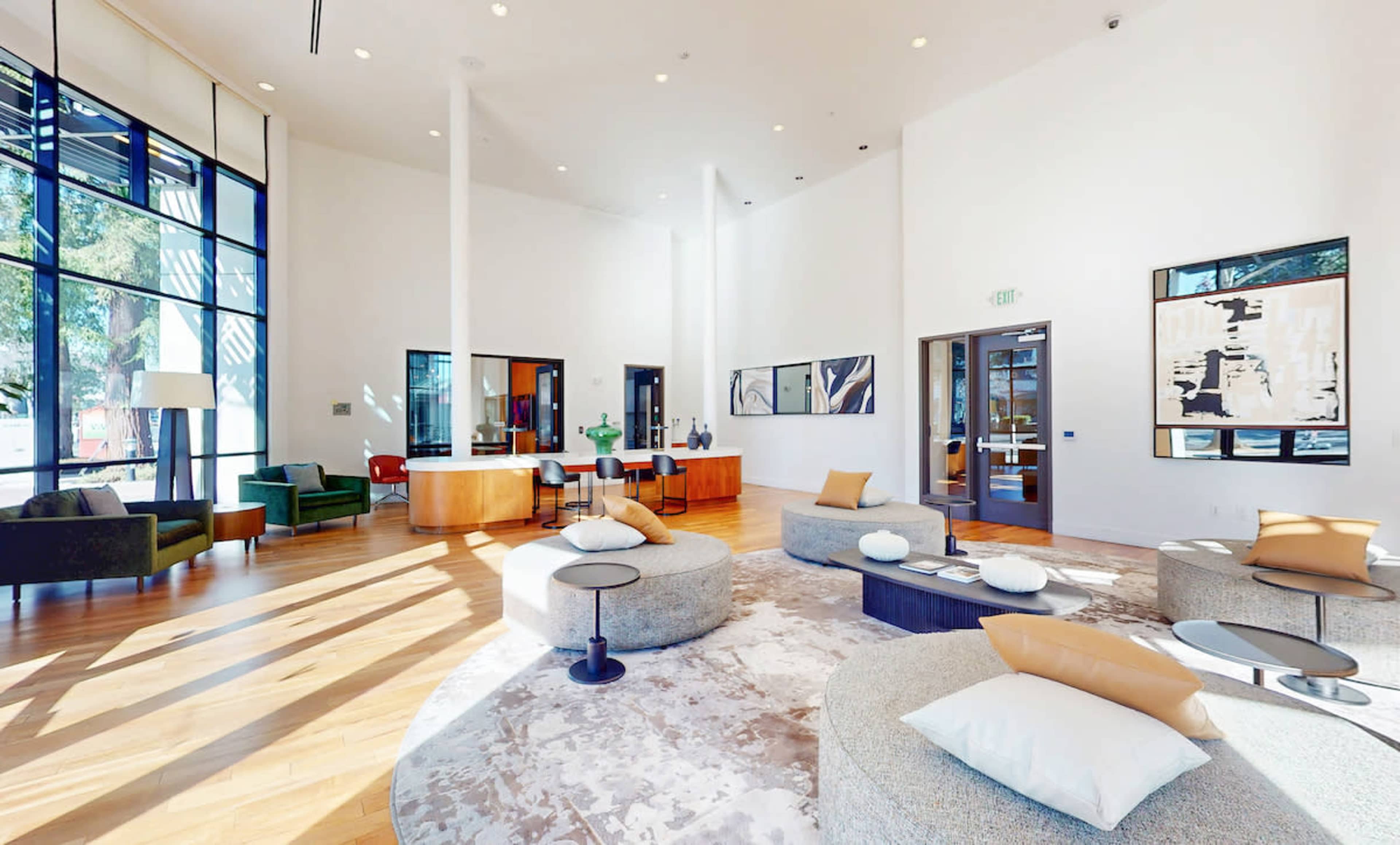 The image shows a contemporary lobby area featuring modern furniture, large windows, and a mix of seating arrangements on a wooden floor.