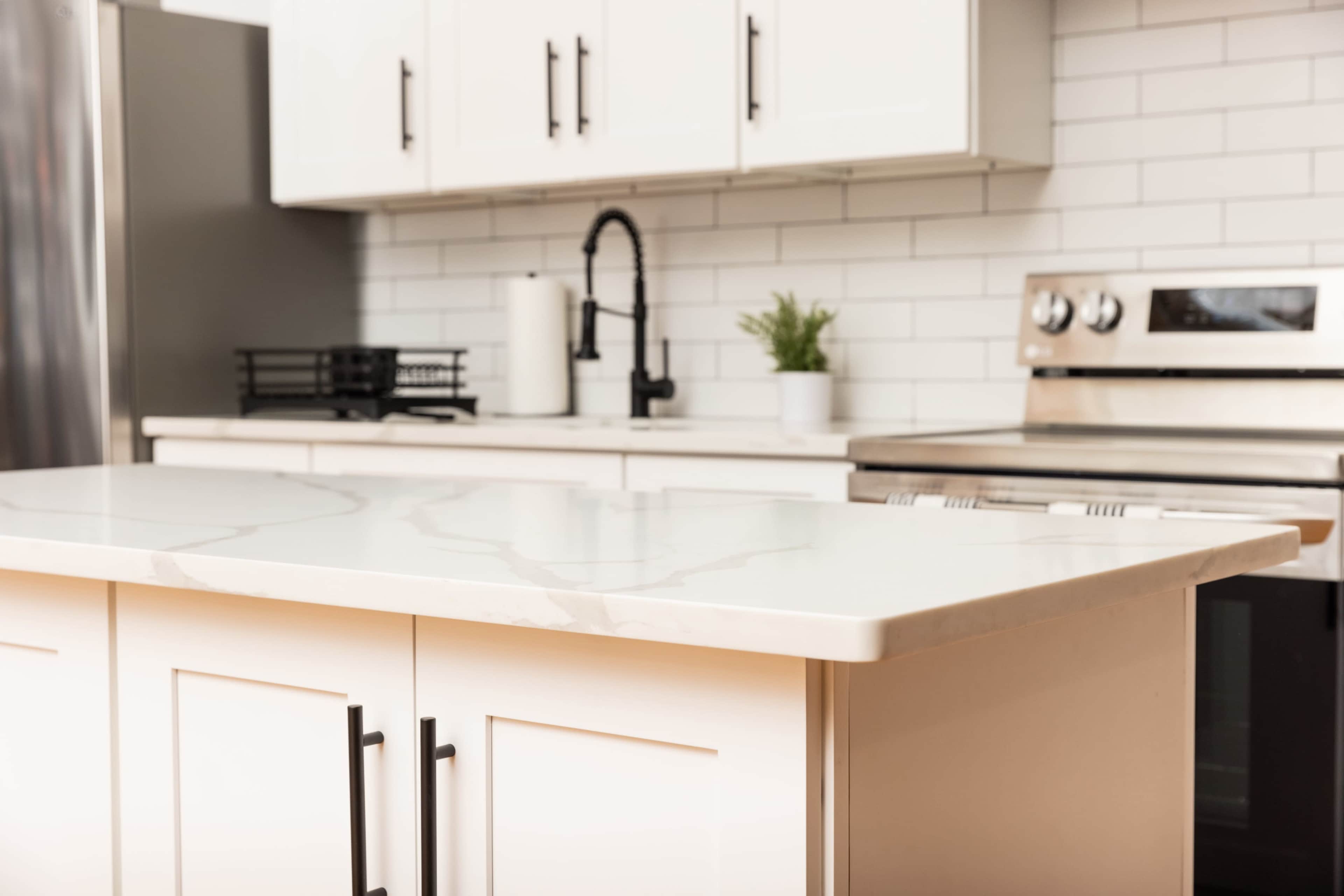 A modern kitchen with a white marble countertop, stainless steel appliances, and minimalistic cabinetry.