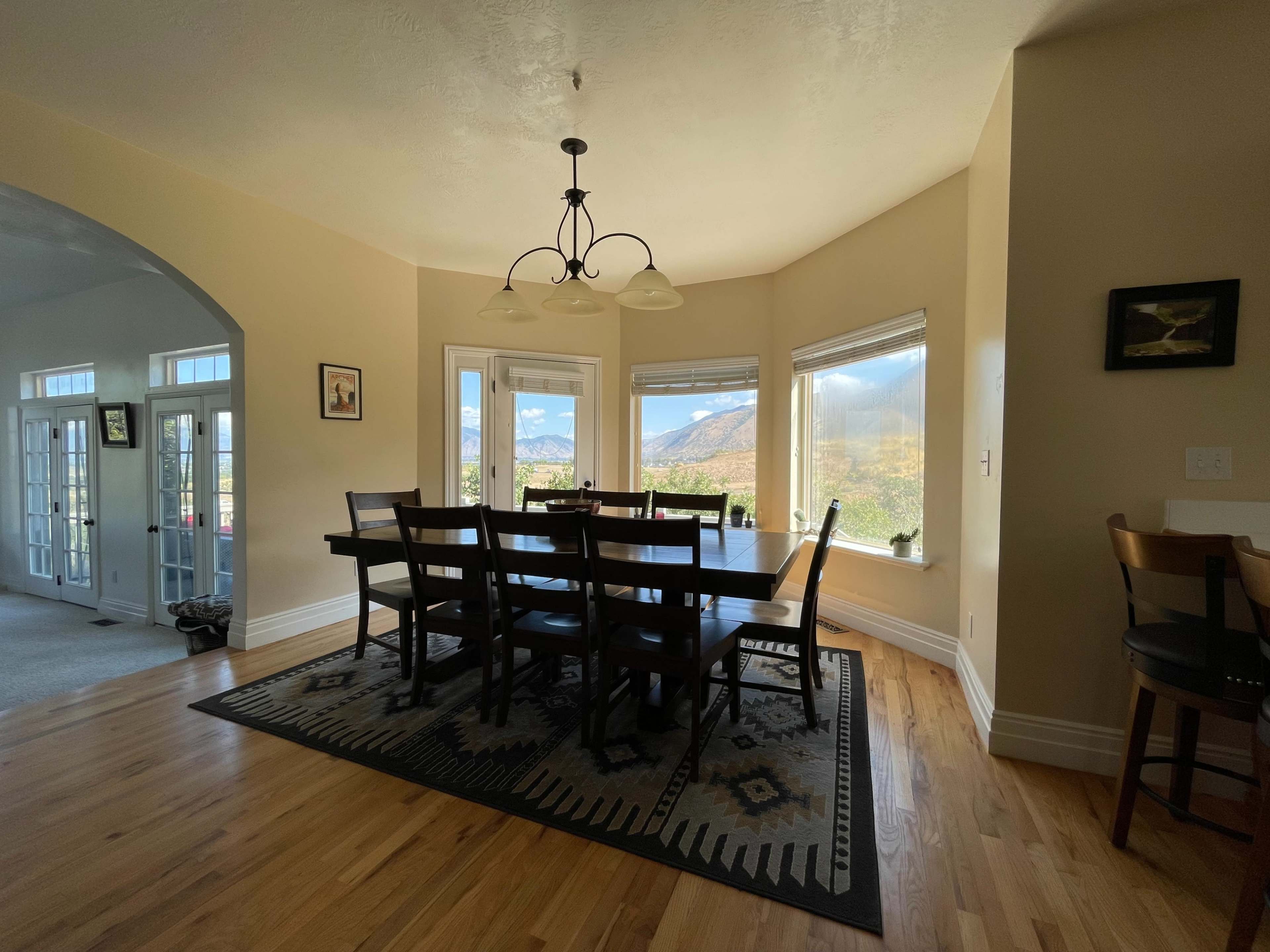 A spacious dining room features a large wooden table surrounded by chairs, with large windows overlooking a mountain view.