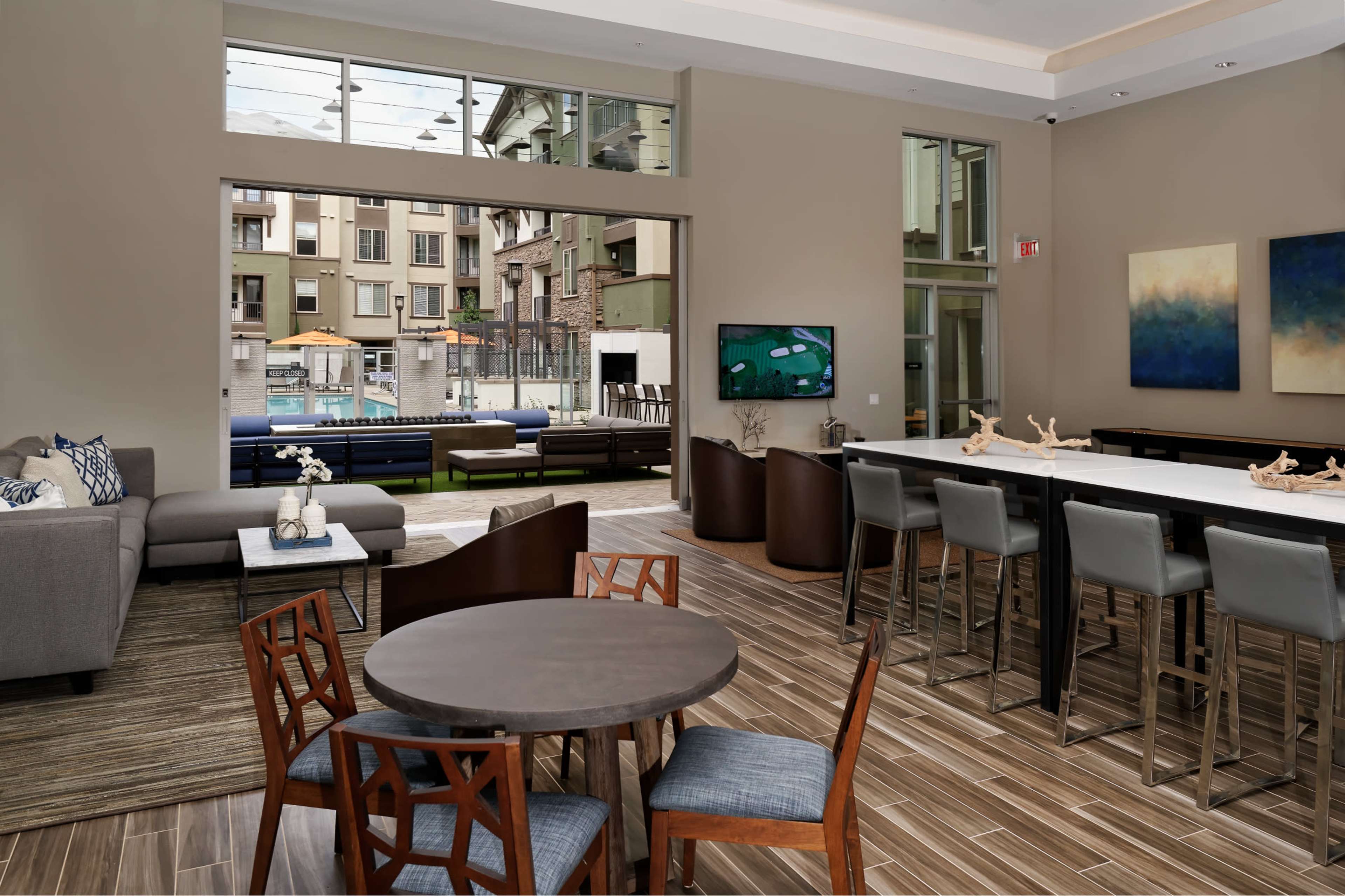 A contemporary lounge area with seating arrangements, a dining table, and a view of a pool through large windows.
