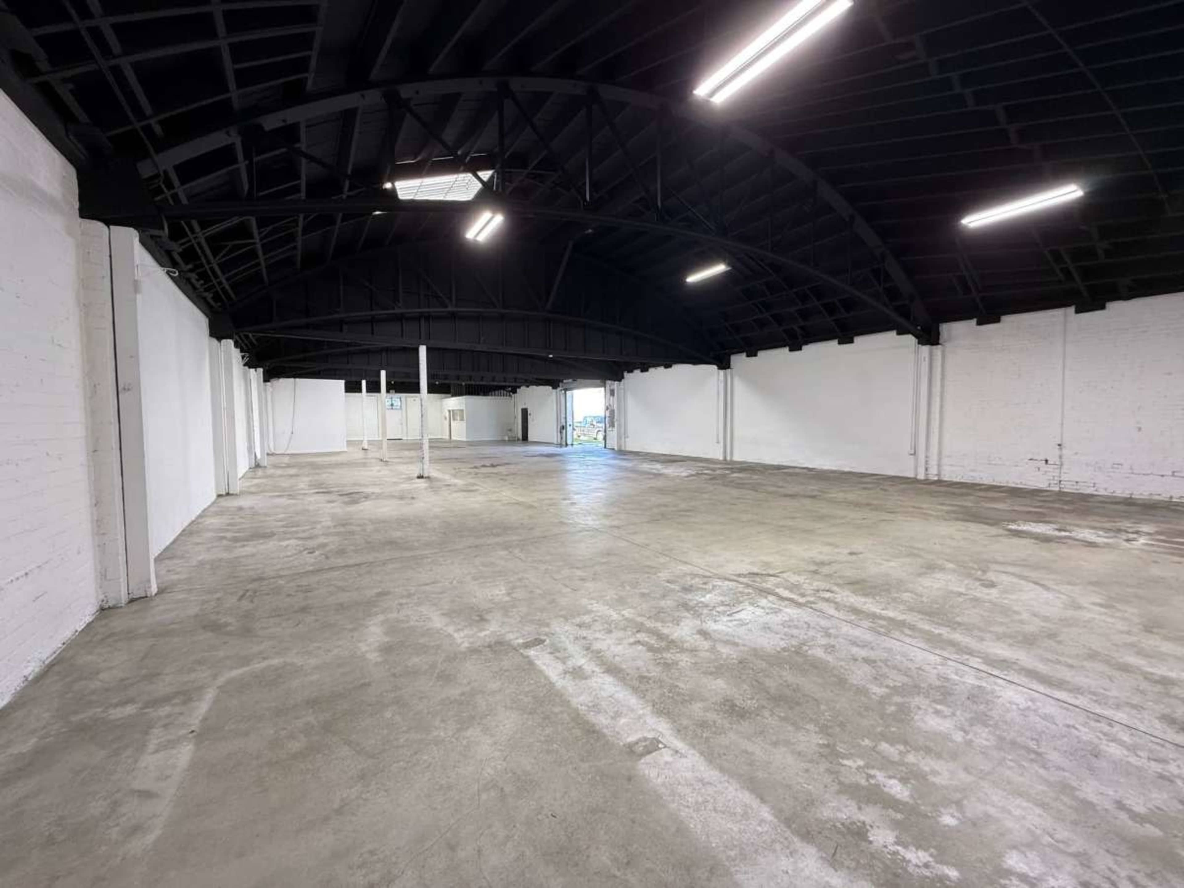 The image shows a large, empty warehouse space with a high black ceiling and polished concrete floors.