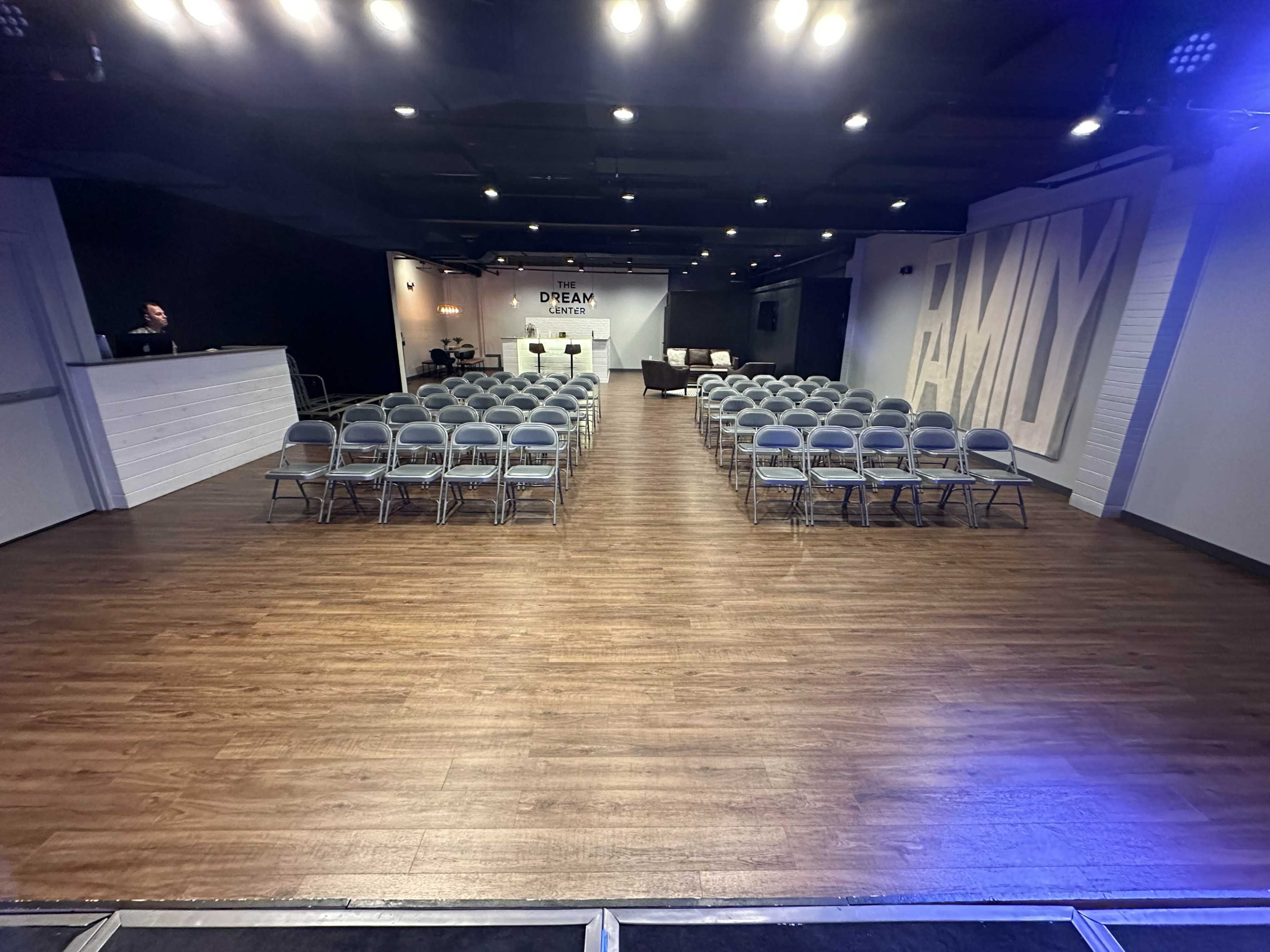 A spacious event room featuring neatly arranged rows of gray chairs facing a stage area with a large backdrop displaying the words "DREAM" and "FAMILY."