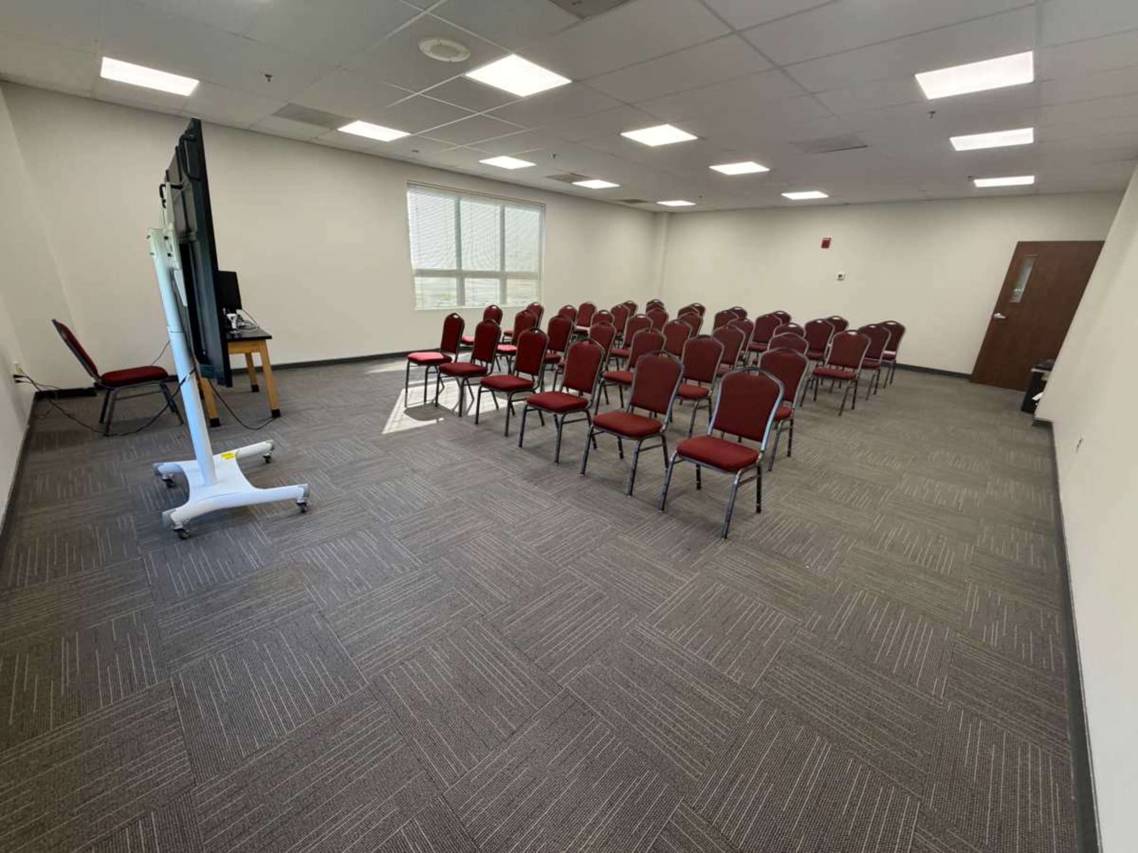 A meeting room is set up with rows of red chairs and a large screen at the front.