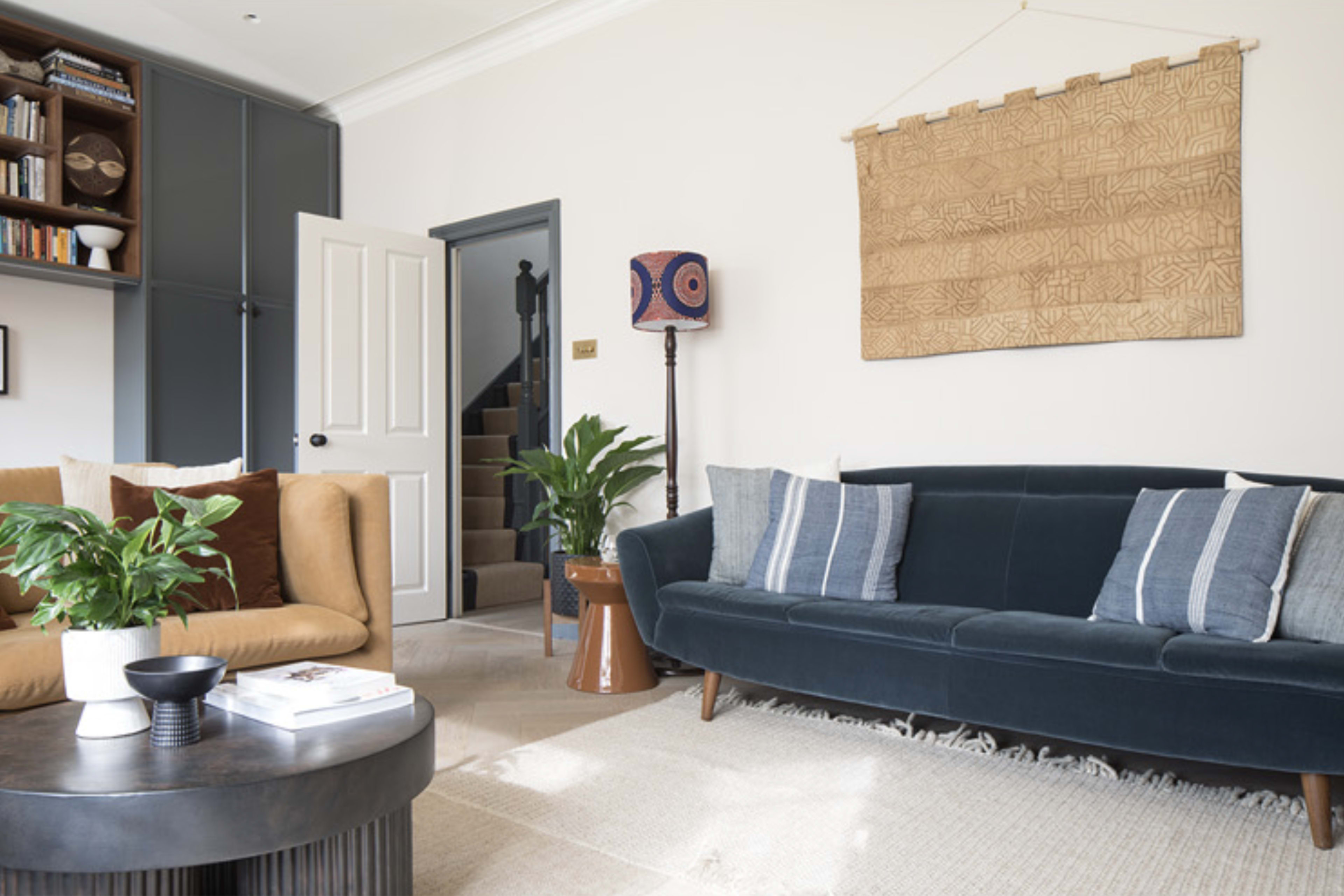 A living room with a dark blue sofa, a tan couch, a round coffee table, a patterned lamp, and a decorative wall hanging.