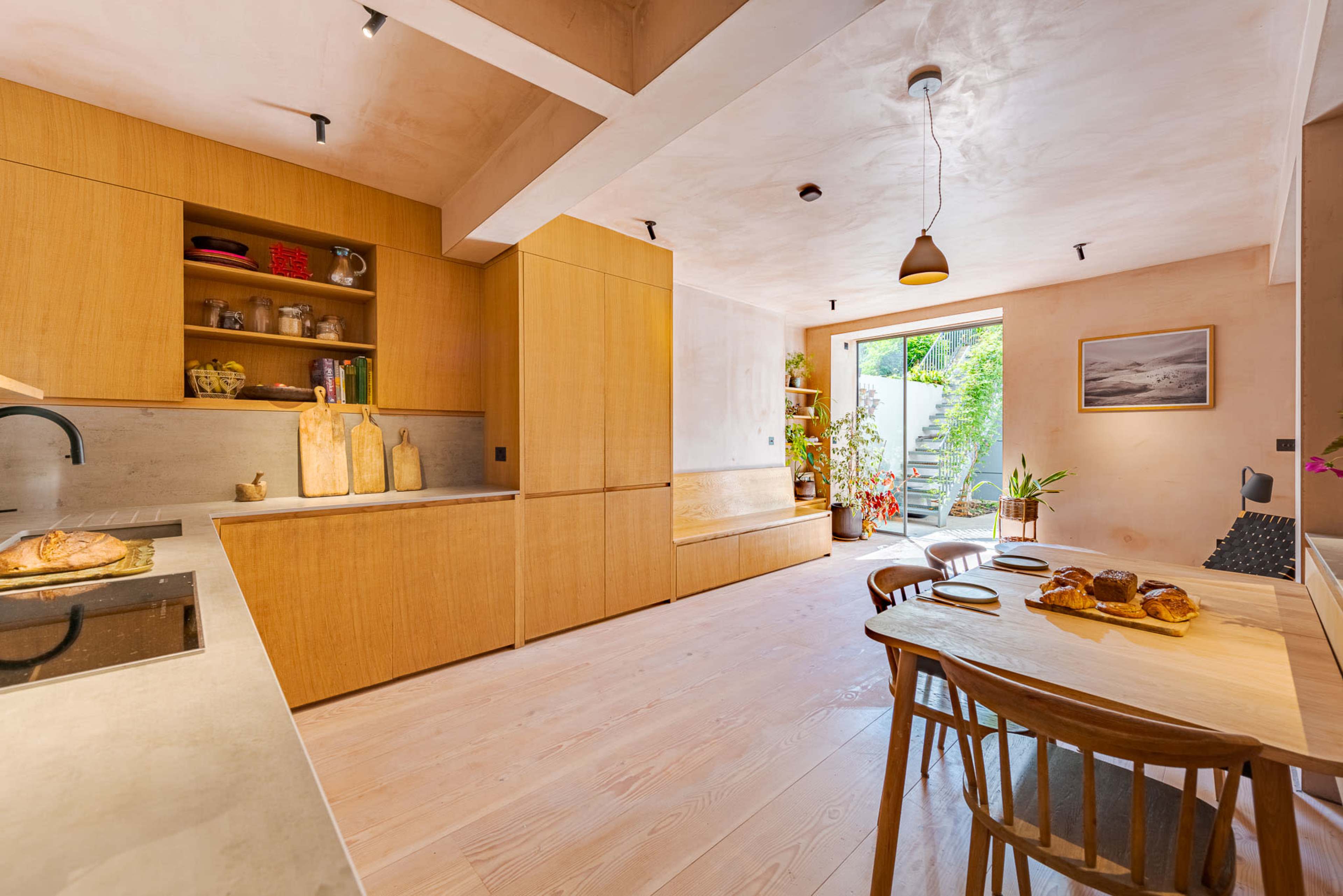 The kitchen features wooden cabinetry, a dining table with baked goods, and a window that opens to a garden area.