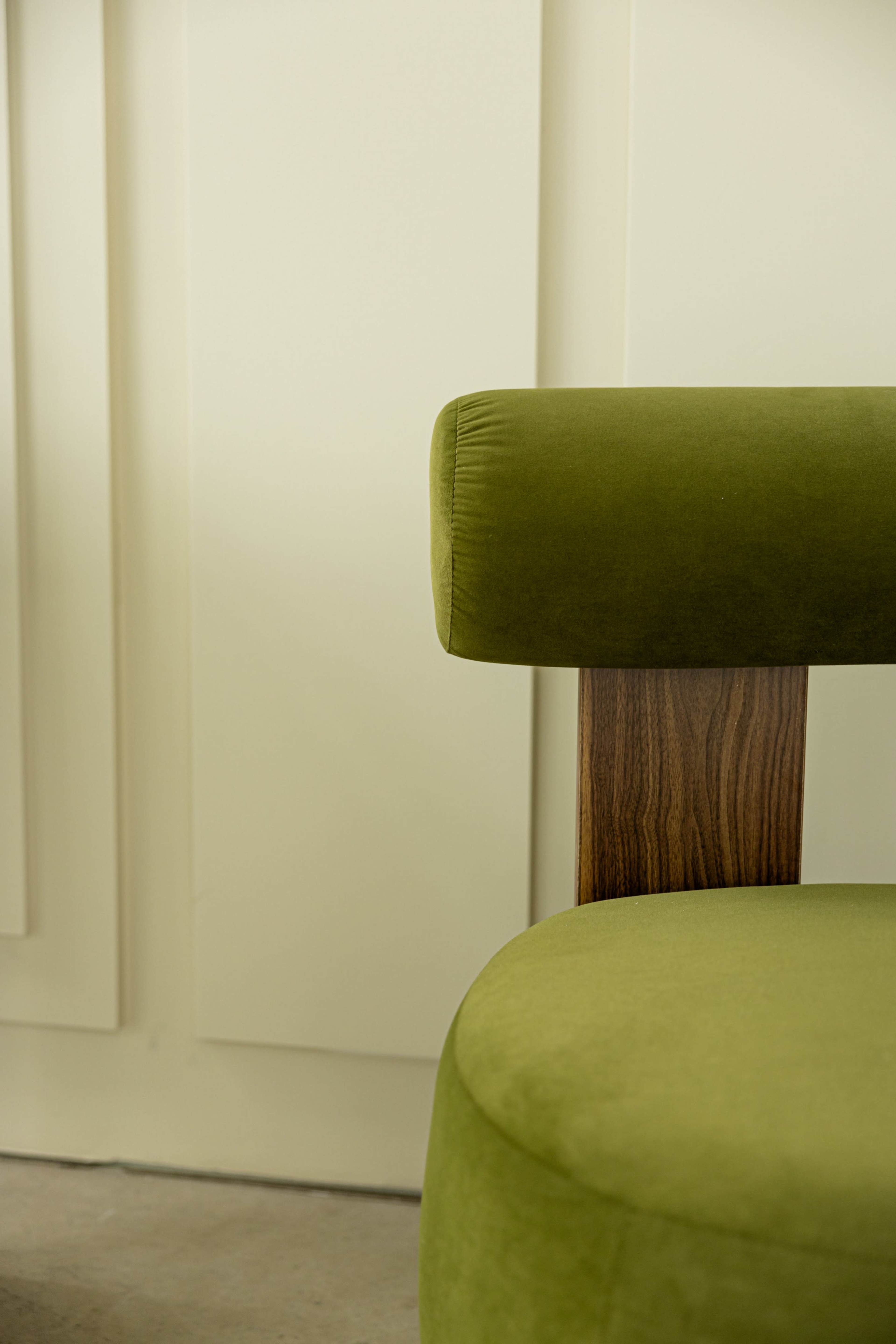 The image features a close-up of a green upholstered chair with a wooden armrest against a plain wall.