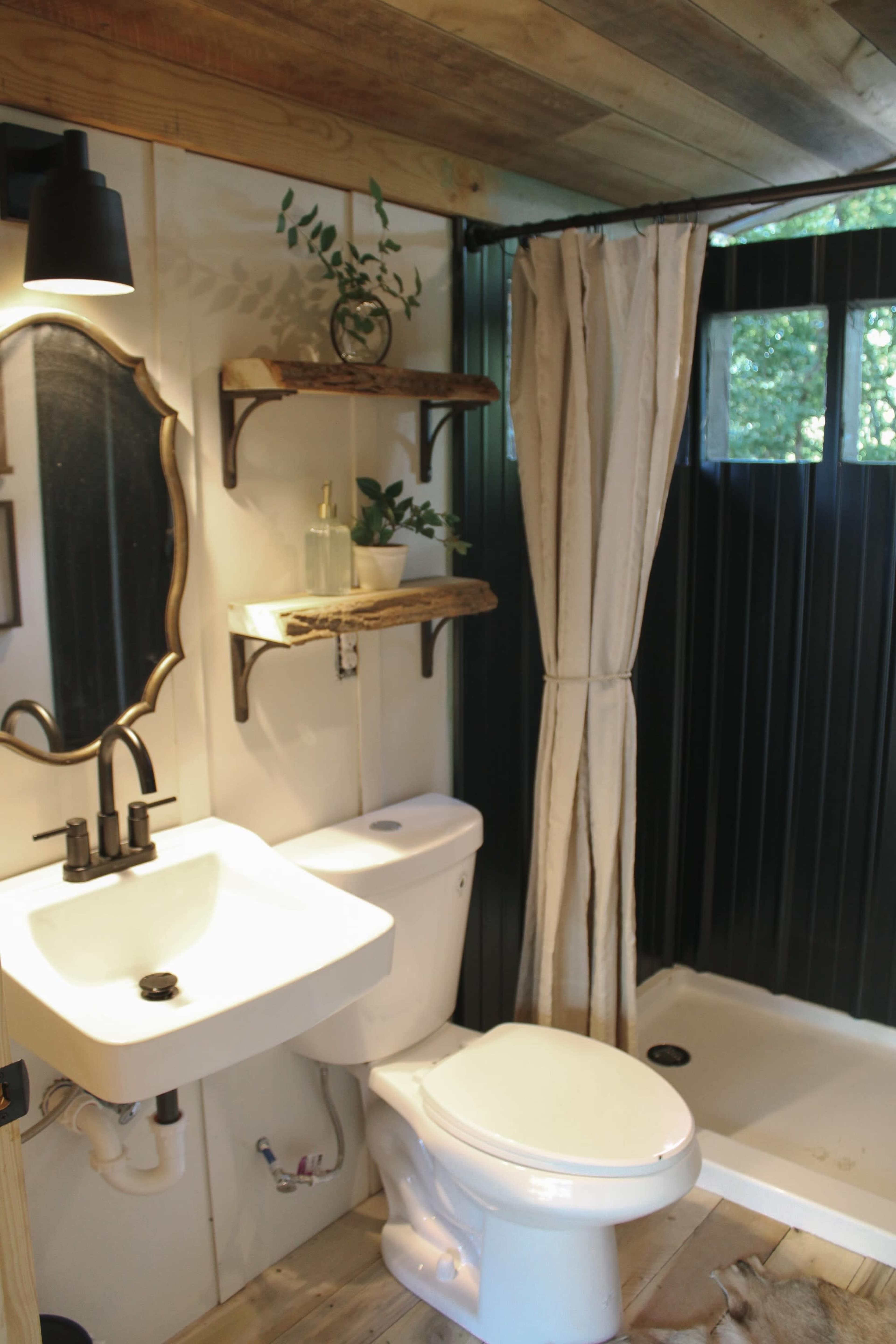 A compact bathroom featuring a toilet, a sink, shelves with decorative items, and a shower area with a curtain.