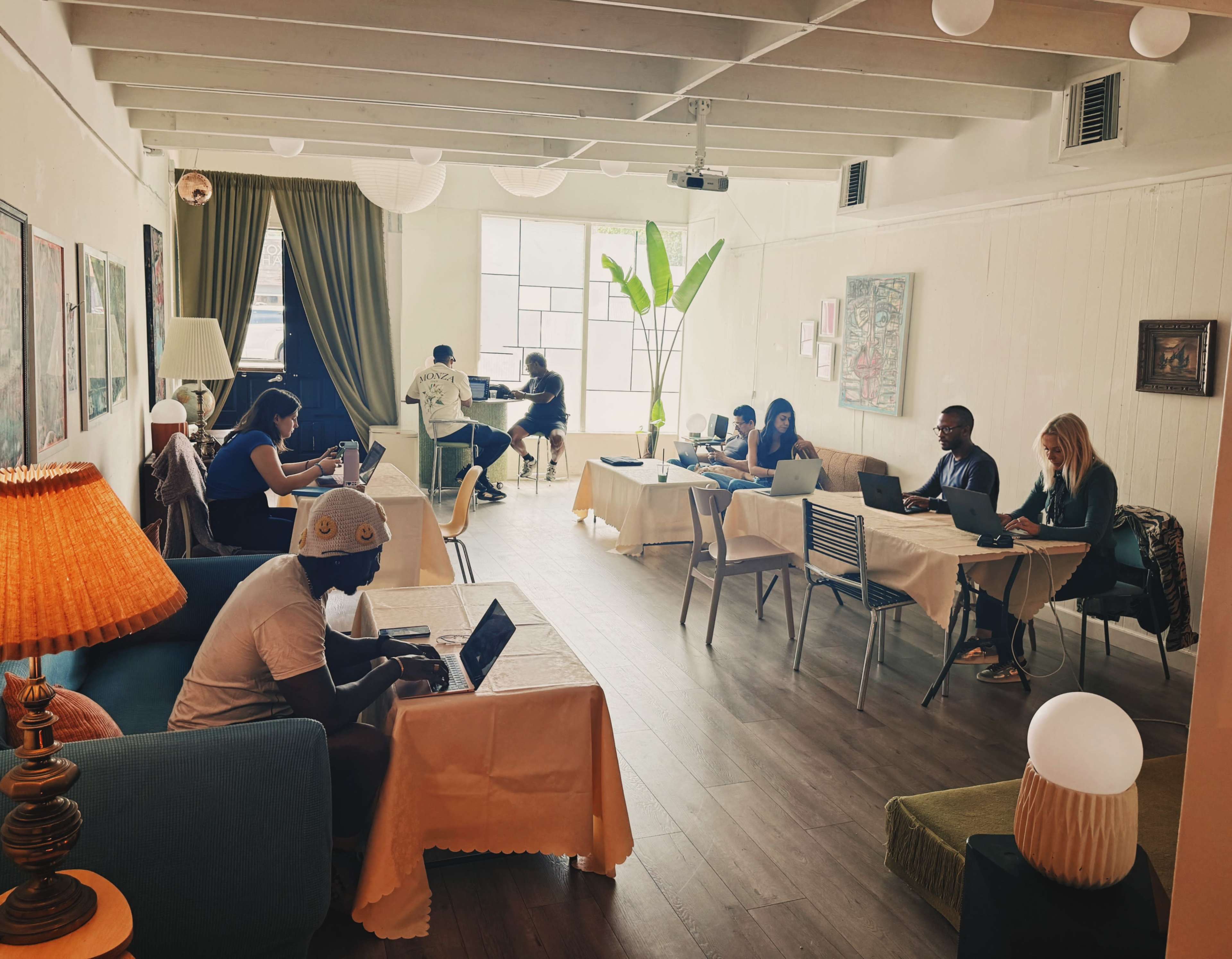 A group of people is working on laptops in a well-lit co-working space with plants and decorative elements.
