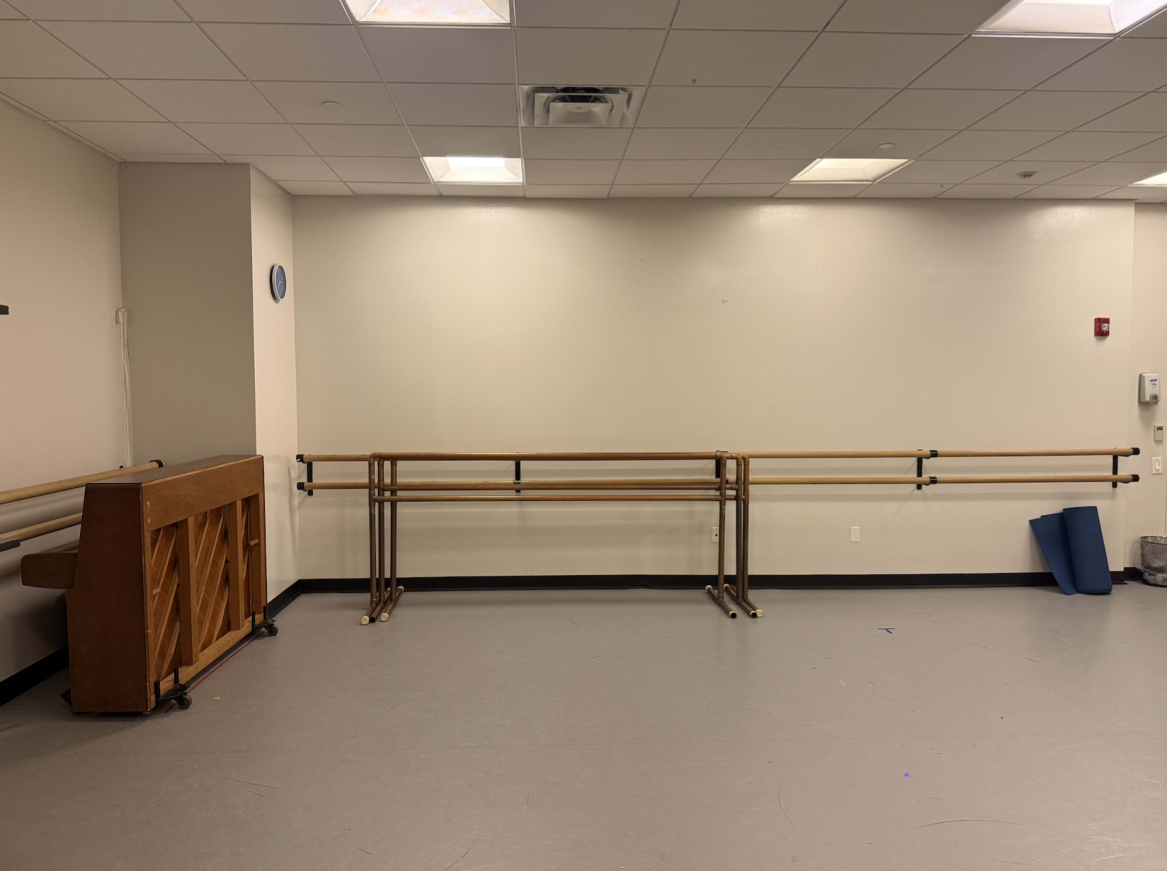 The image shows an empty dance studio equipped with wooden ballet barres and a piano against one wall.