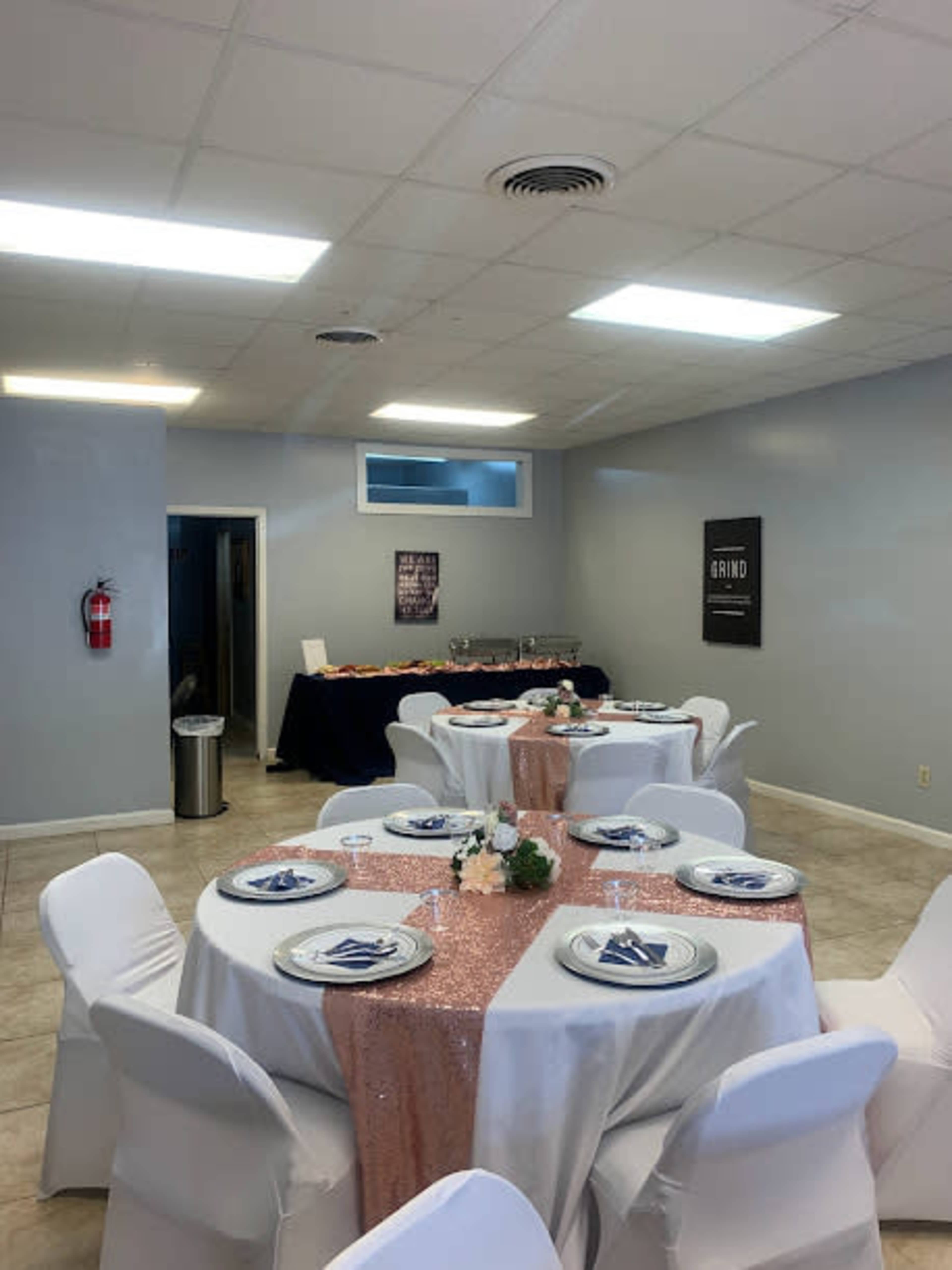 A banquet room with circular tables covered in white tablecloths and a pink sequined centerpiece, along with a buffet table in the background.