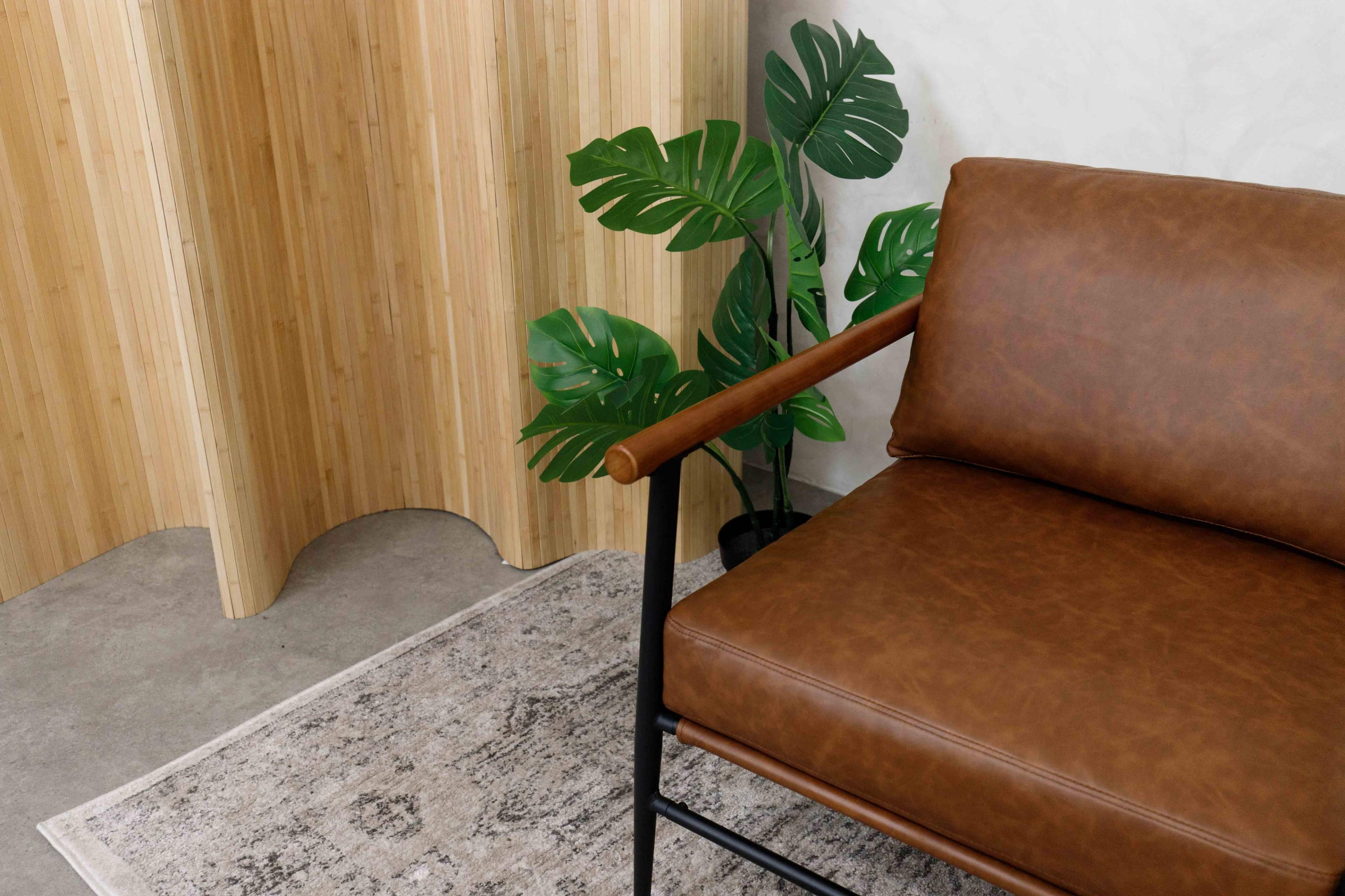 The image shows a brown leather chair next to a green plant, with a bamboo screen in the background.