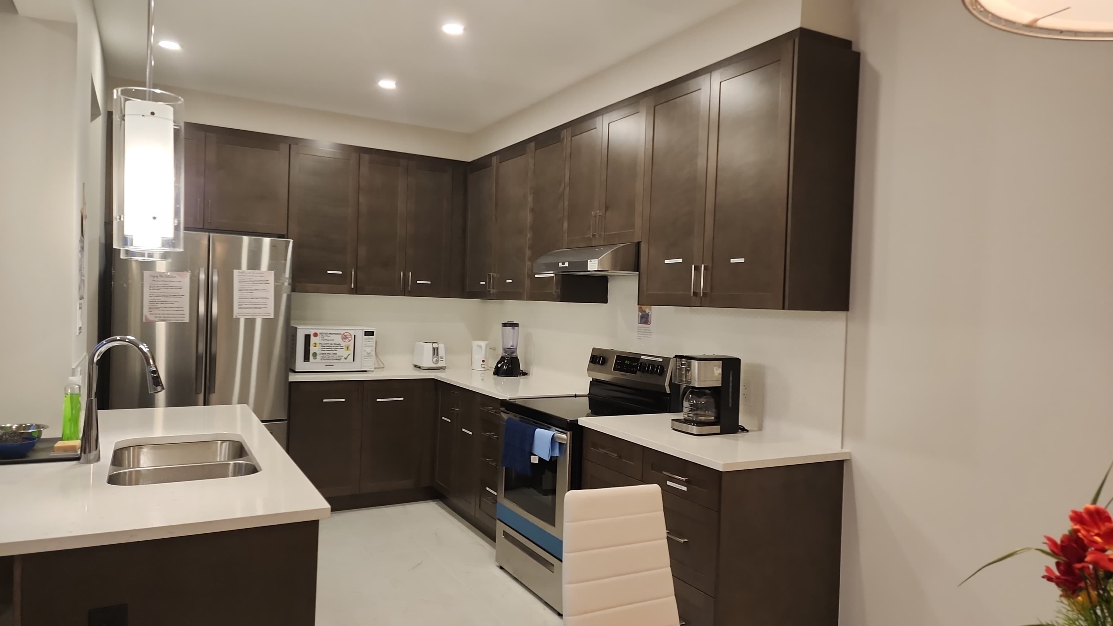 The image shows a modern kitchen with dark wood cabinetry, stainless steel appliances, and a white countertop.