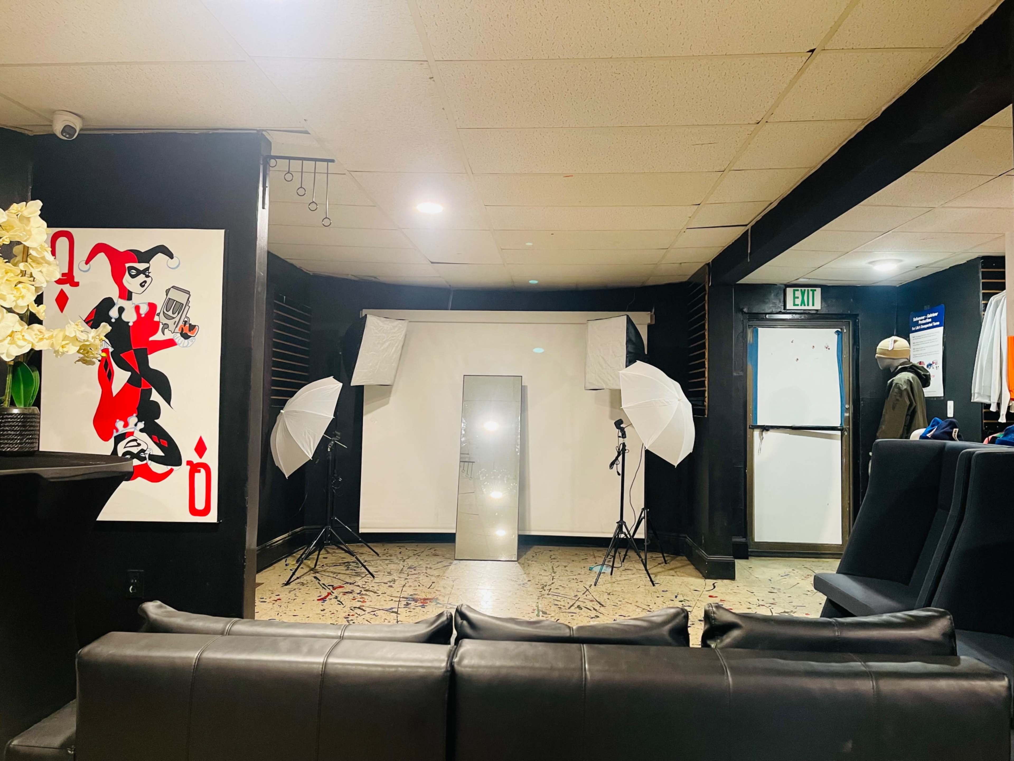The image depicts a photography studio setup featuring two softbox lights, a large mirror, and a white backdrop, along with a black couch and wall art.