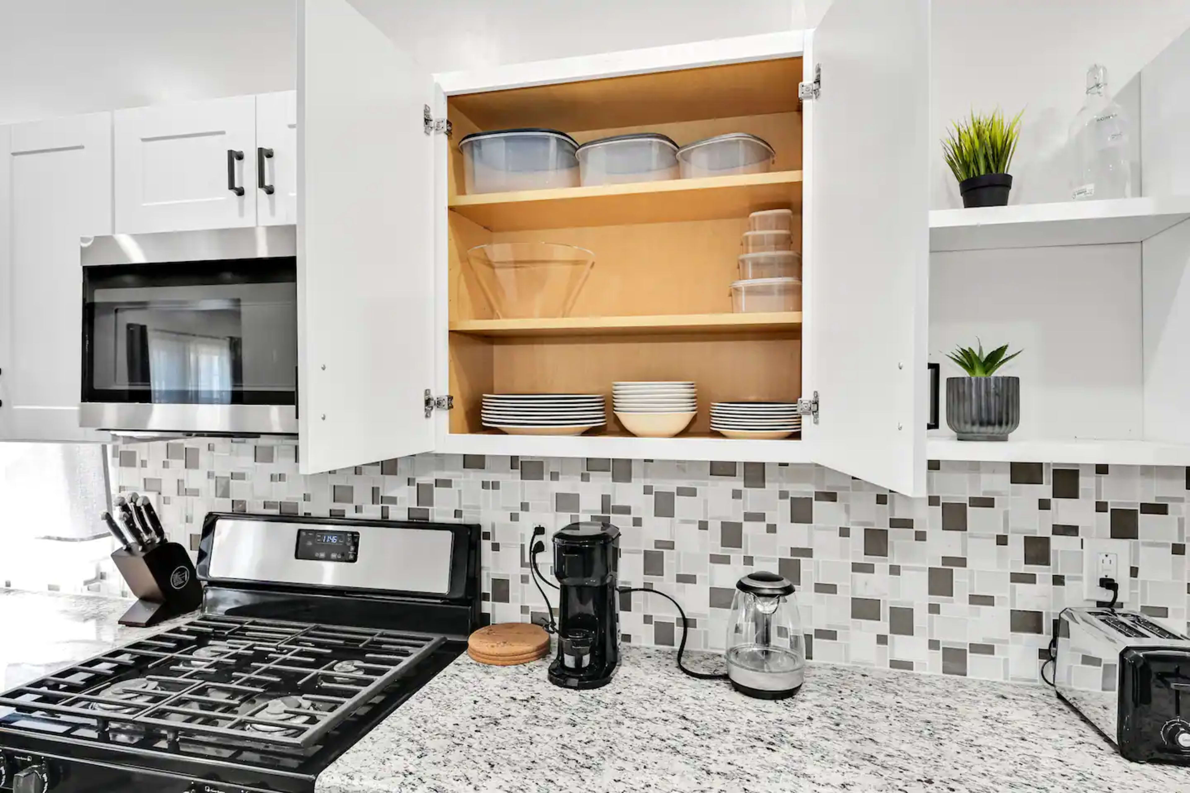 A kitchen cabinet is open, revealing stacked plates and bowls, with a coffee maker and a microwave visible on the countertop.