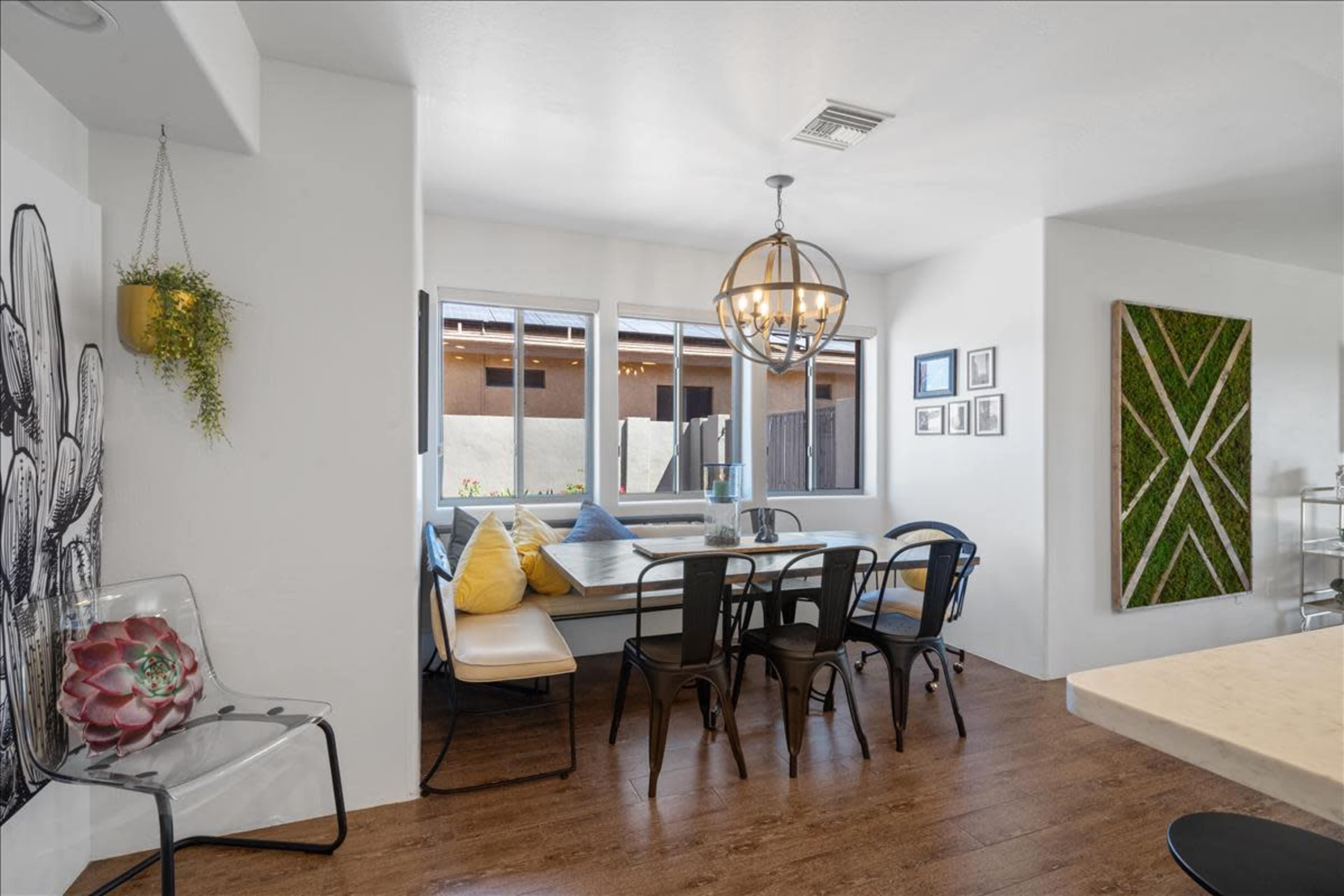 A dining area features a large table surrounded by chairs, with windows overlooking a patio and decorative wall art.