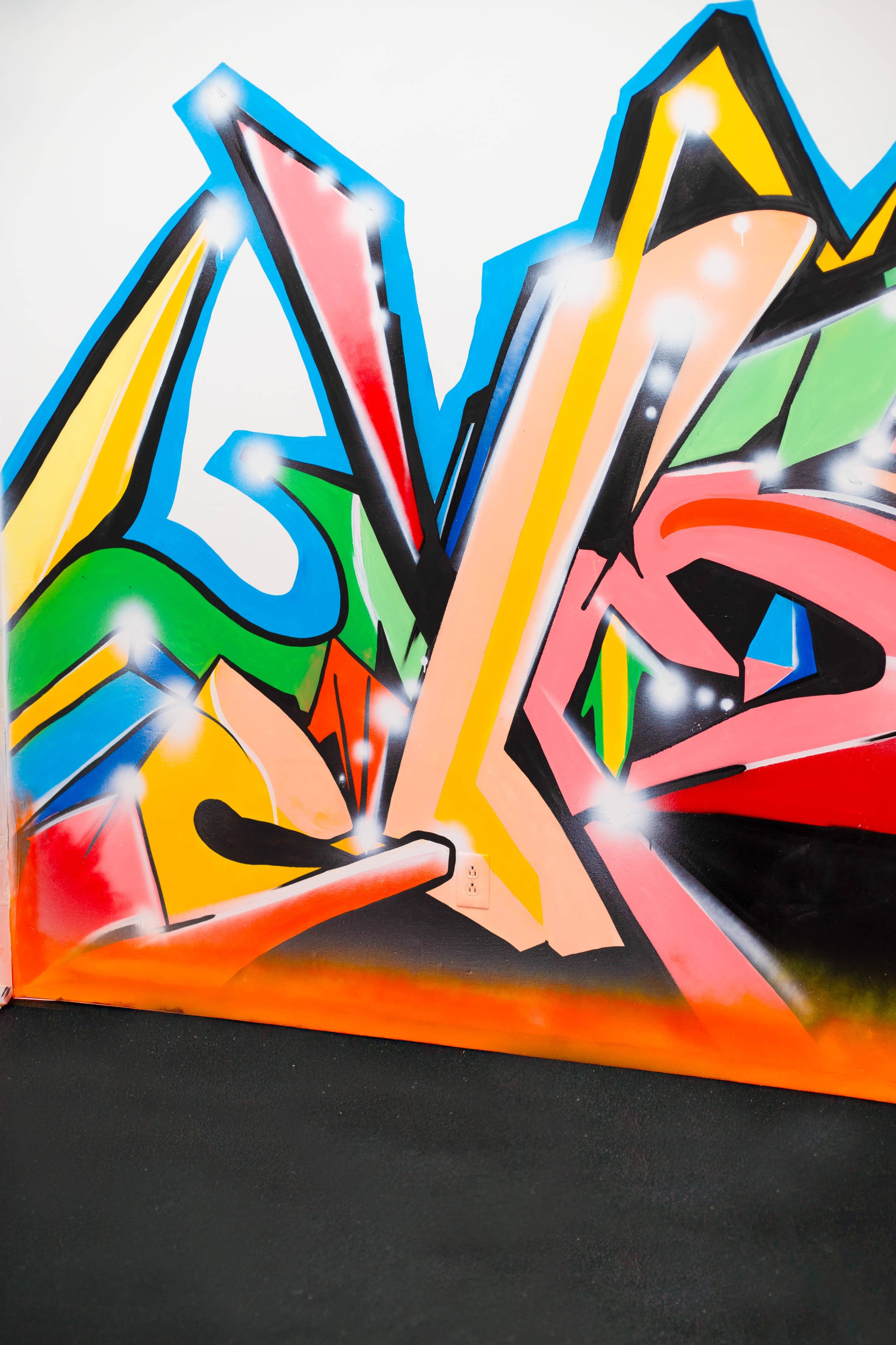 The image features a vibrant graffiti mural with abstract shapes and a blend of colors including red, green, yellow, and blue.