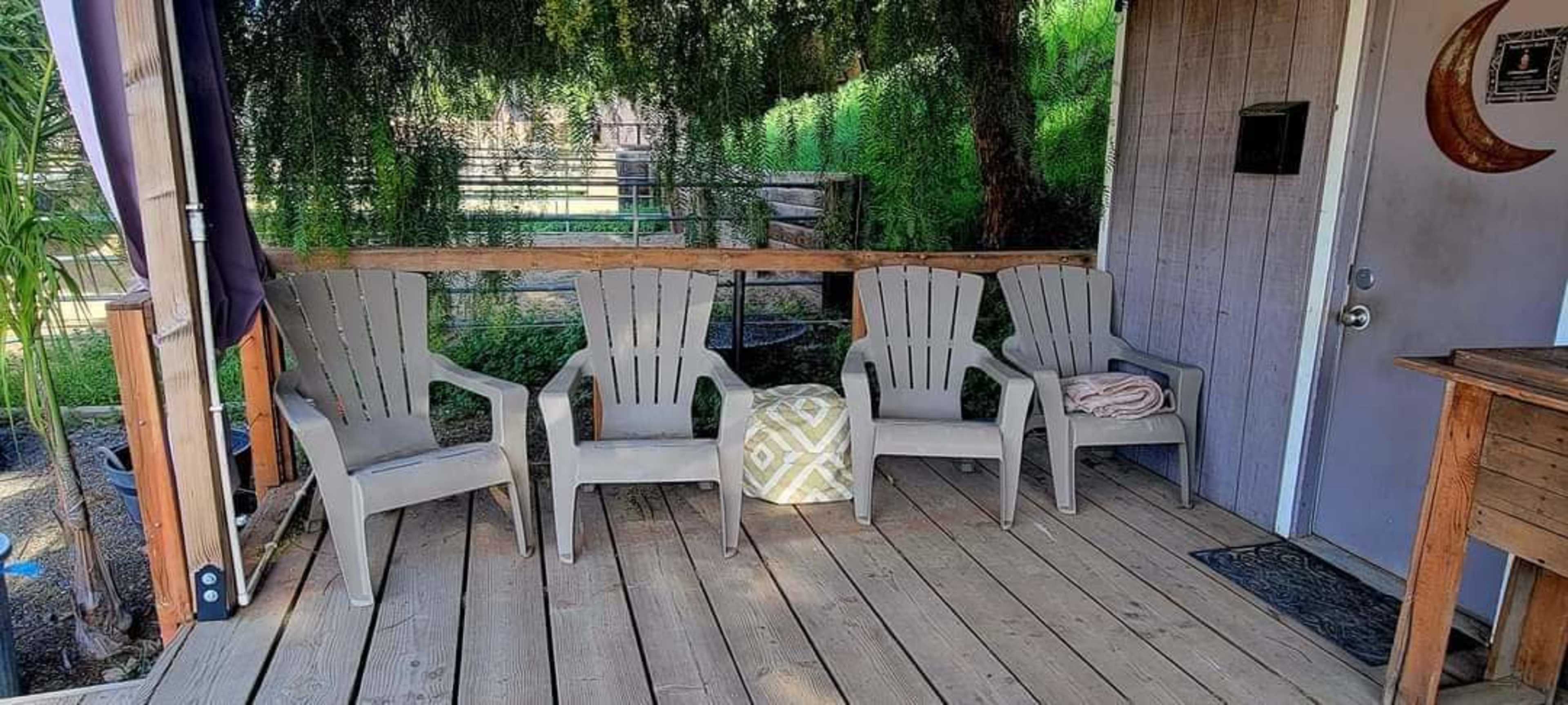 A covered porch features four gray chairs arranged around a decorative pillow on a wooden deck.