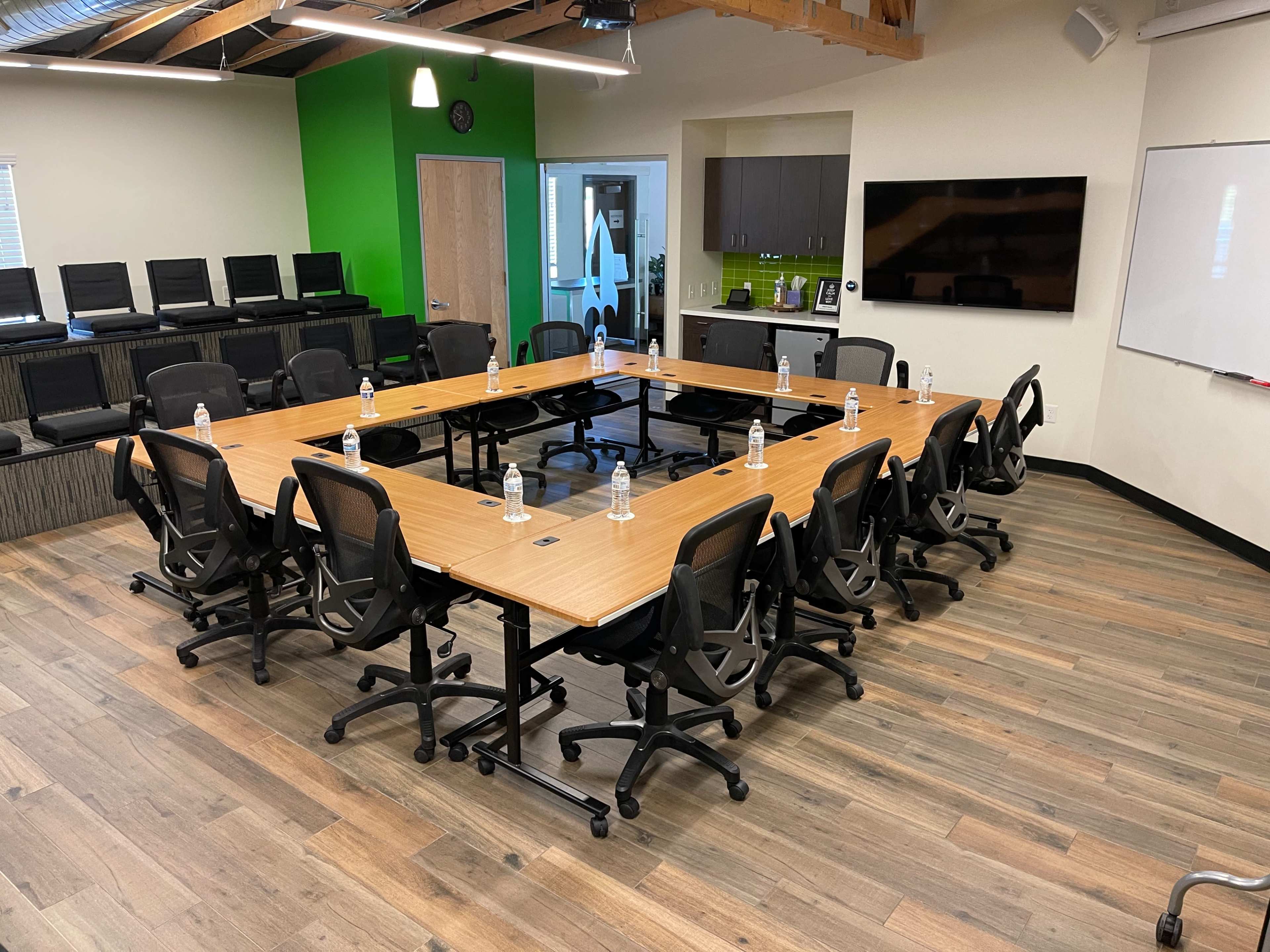 A conference room features a large rectangular table surrounded by ergonomic chairs, with water bottles placed at intervals on the table.