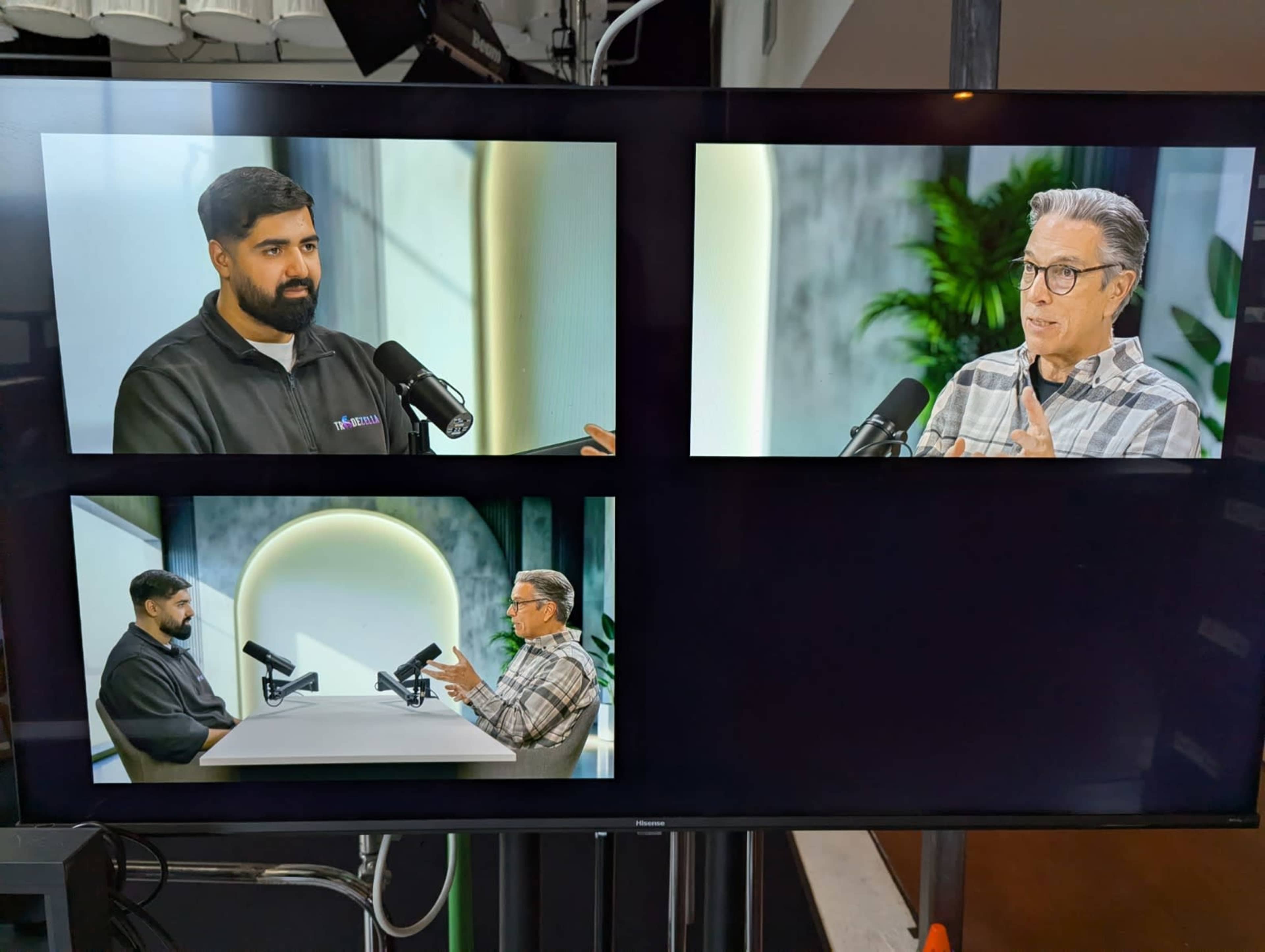 The image shows a screen divided into four sections, featuring two men engaged in a discussion, with one in a black jacket and the other in a plaid shirt, both using microphones in a studio setting.