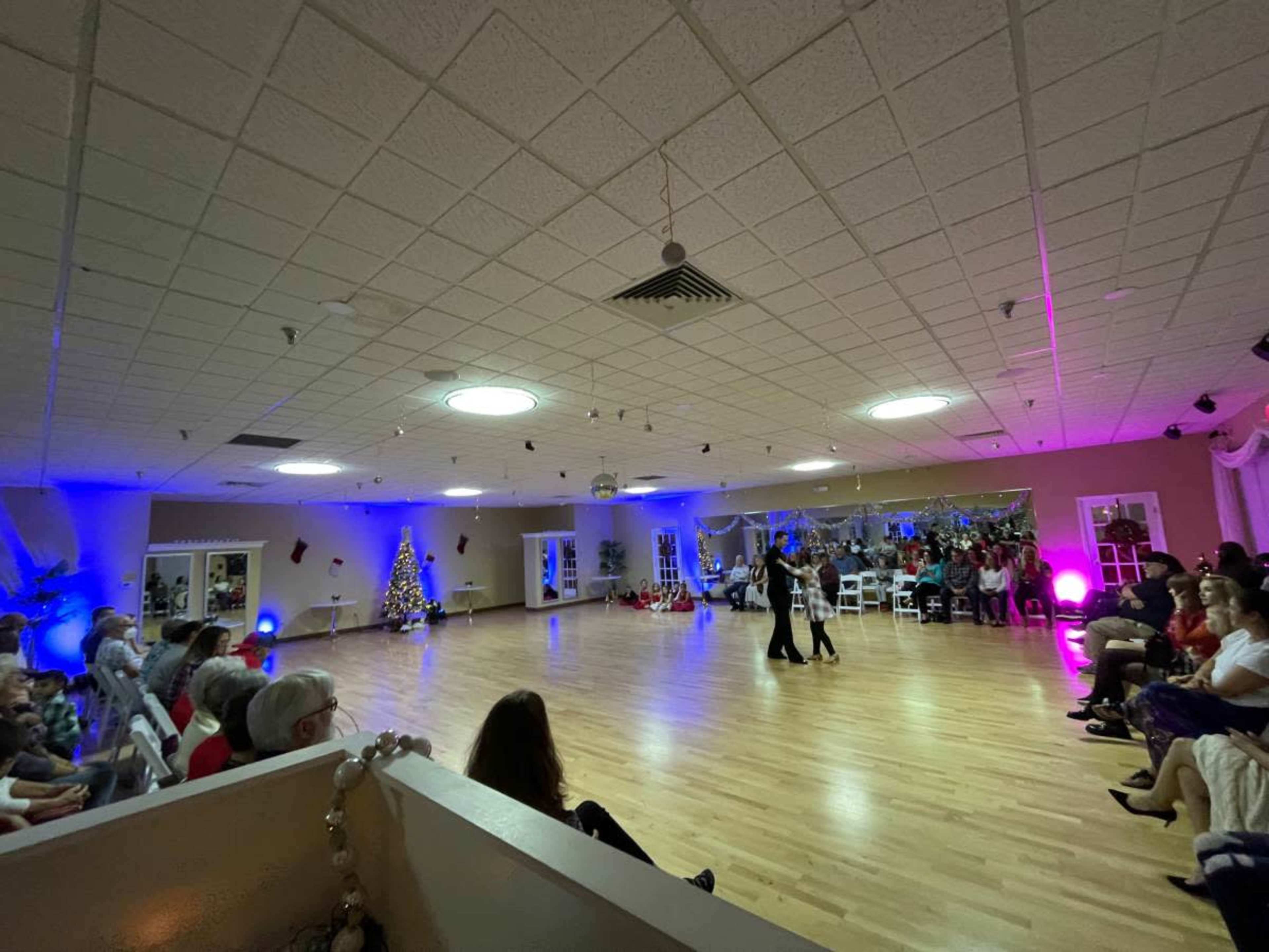 A group of people is watching a dance performance in a well-lit indoor space decorated for the holiday season.