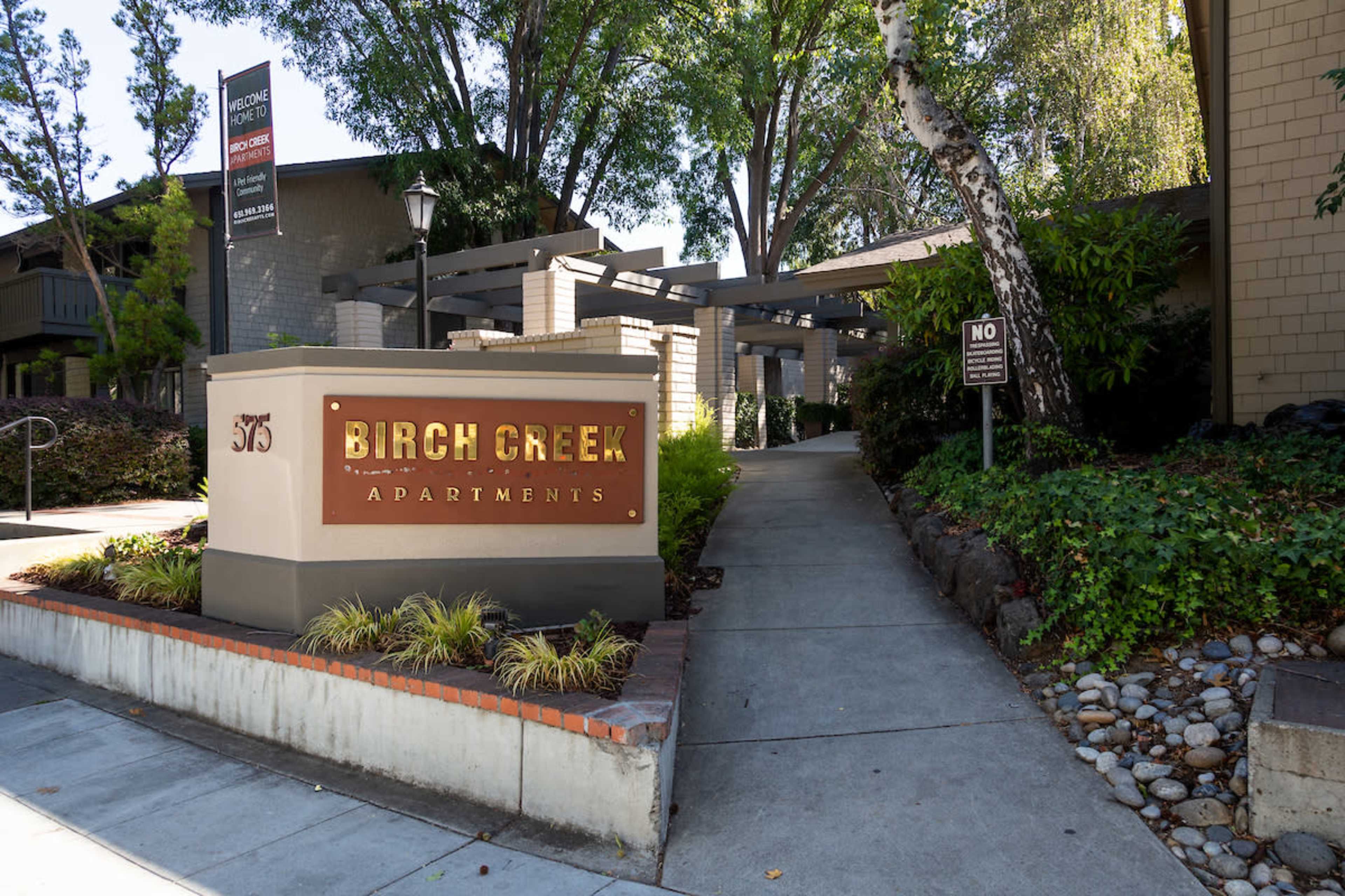 The entrance to Birch Creek Apartments features a sign with the name prominently displayed alongside landscaped pathways and greenery.